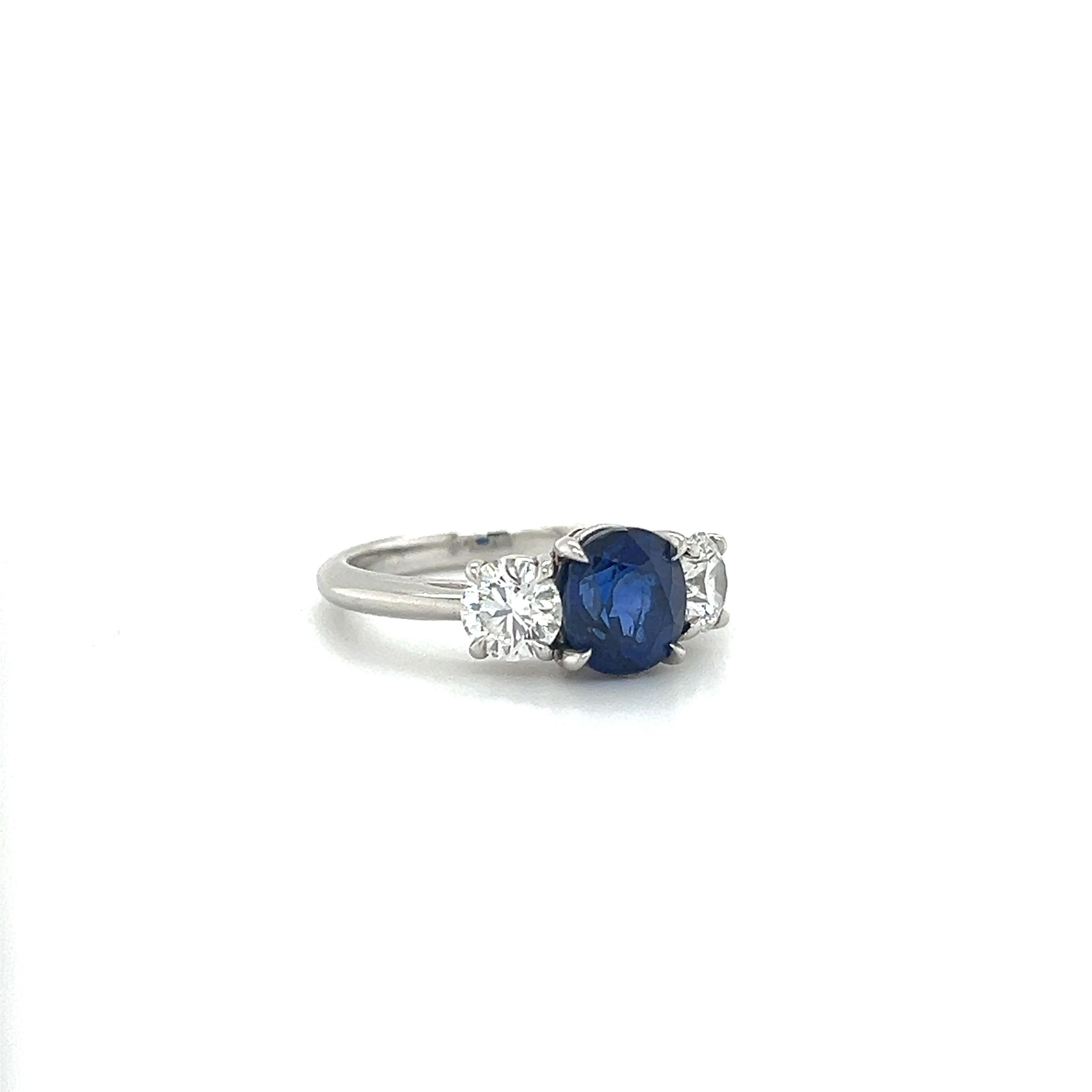 Beautiful hand crafted ring by famed designer Tiffany & Co. The ring is made platinum and highlights a three stone design. The center stone is one blue colored sapphire gemstone. The sapphire displays a vibrant blue color and contrasts perfectly