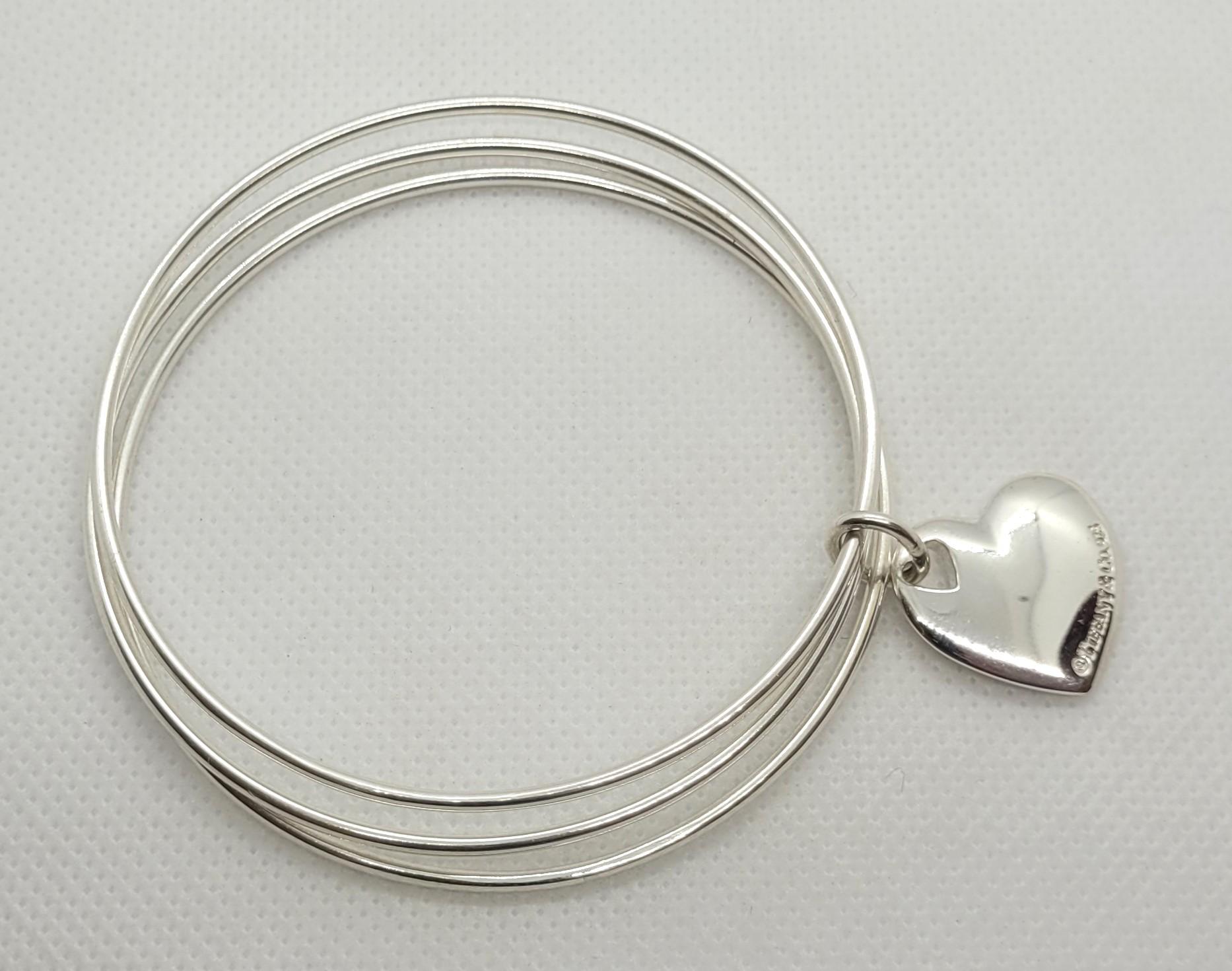 Beautiful Tiffany & Co silver trio bangle bracelet with engravable heart charm. The bracelet is a standard size for average-sized ladies' wrists. The diameter of the three bangles is a total of 2.5+ inches. The width of each bangle is 1.8mm with a