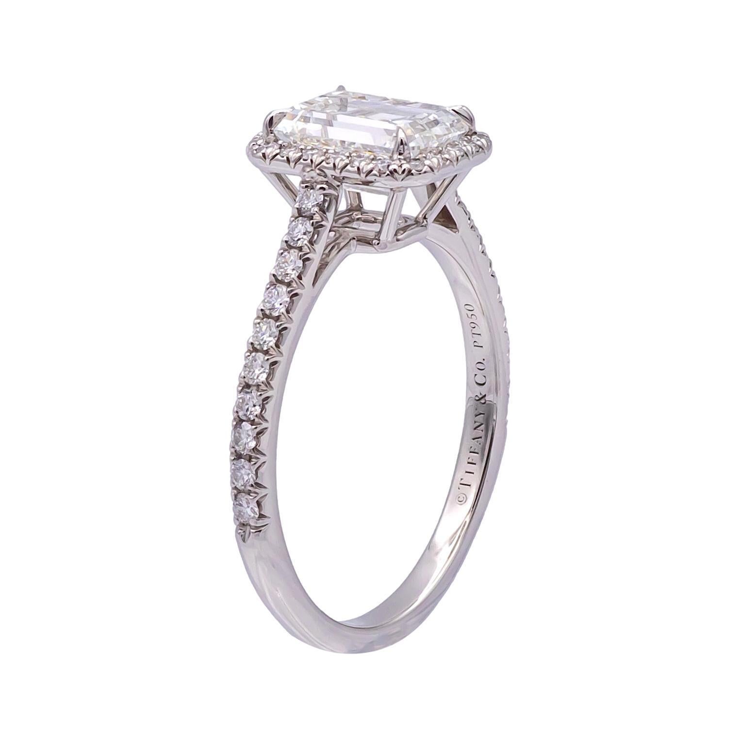 This stunning Tiffany & Co. Soleste engagement ring features a 1.38 carat emerald-cut diamond as the centerpiece, graded H in color and VS1 in clarity. The diamond is set in platinum and surrounded by a diamond halo of round brilliant-cut diamonds,