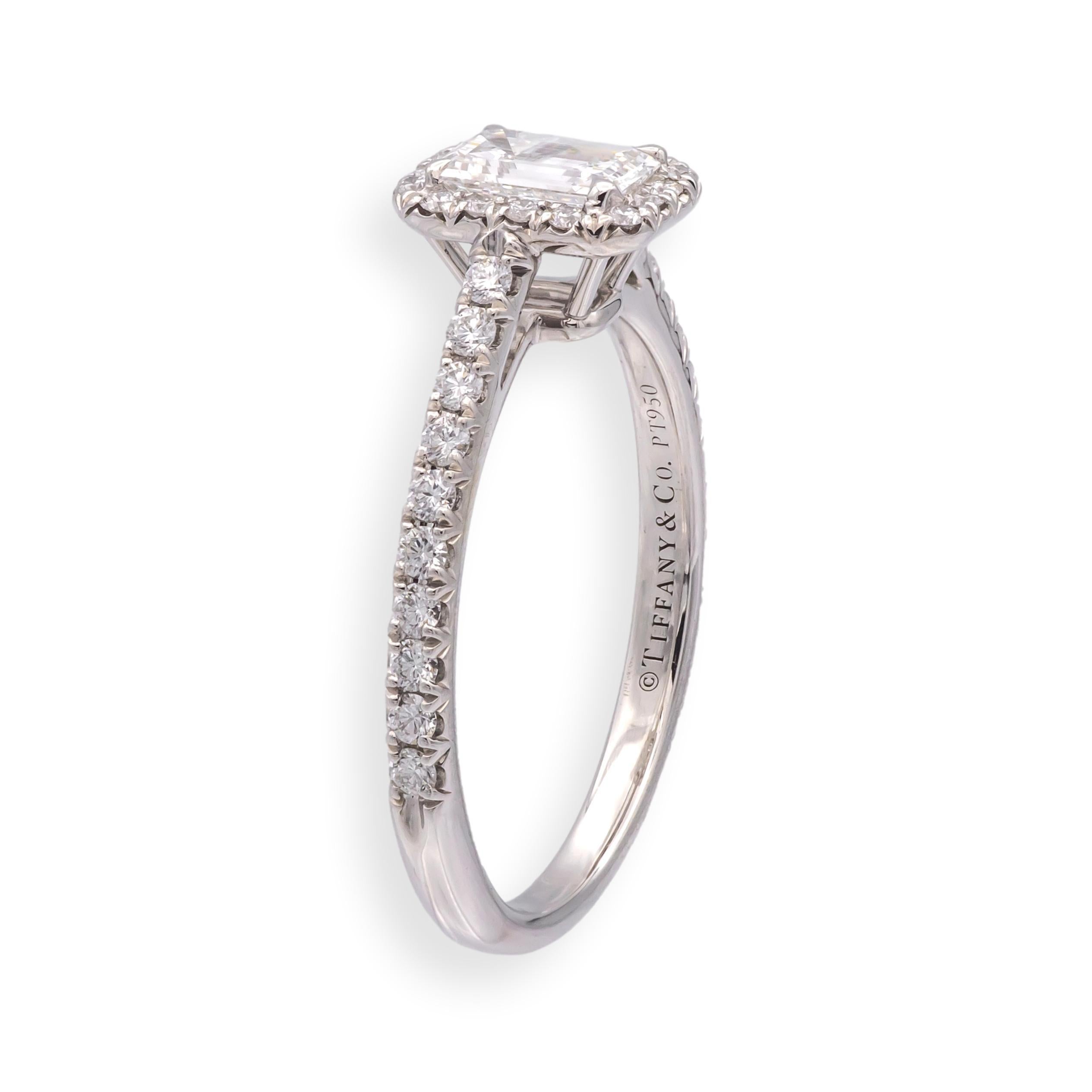 This Tiffany & Co. Soleste engagement ring features a center emerald-cut diamond weighing approximately 0.45 carats, framed by a halo of round brilliant diamonds. Crafted in platinum, the setting is designed to enhance the brilliance of the center