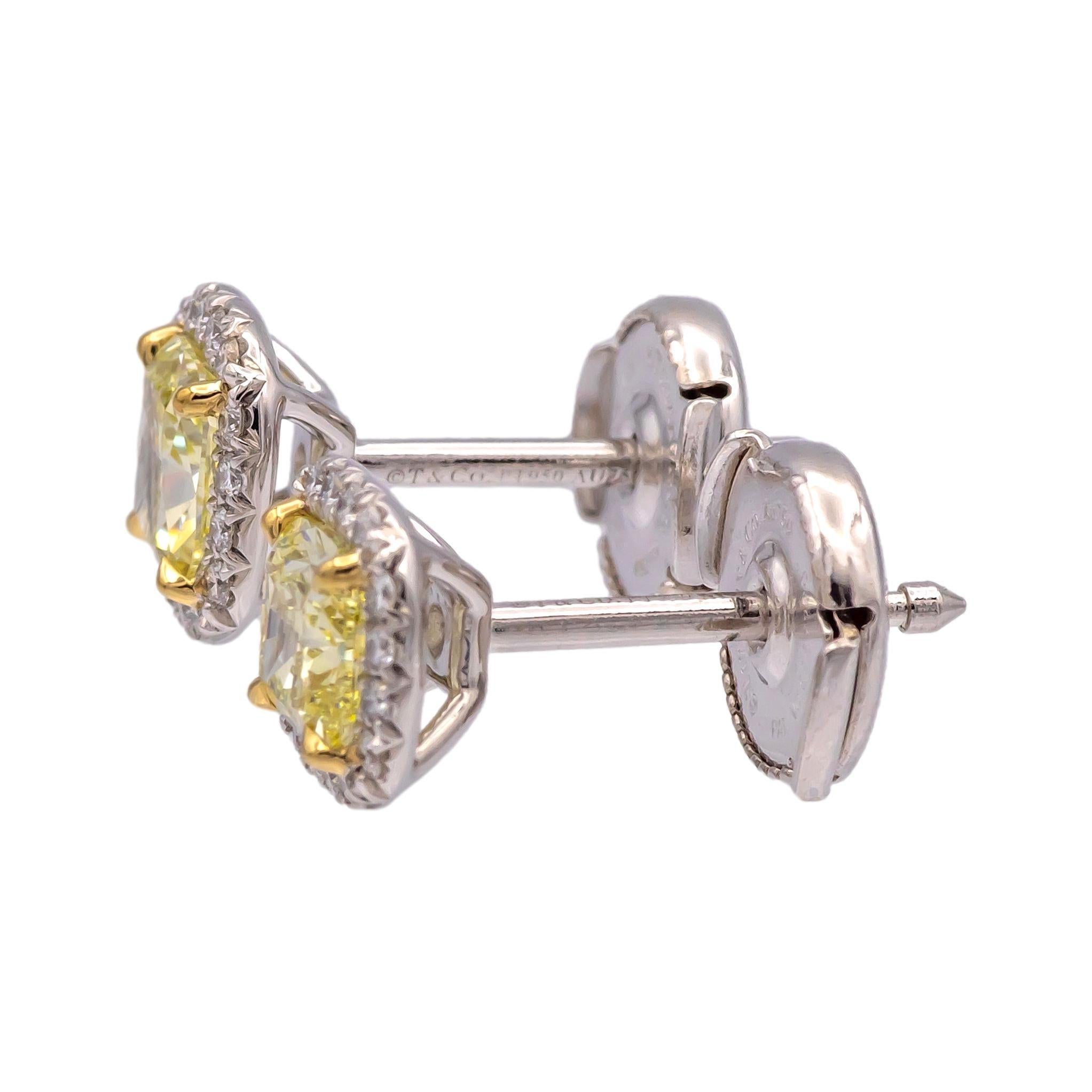 These Tiffany & Co. Soleste Halo Stud Earrings feature two fancy yellow cushion-cut diamonds, surrounded by a halo of brilliant-cut white diamonds. The earrings are crafted in platinum (Pt950) and 18K yellow gold (Au750), showcasing Tiffany's