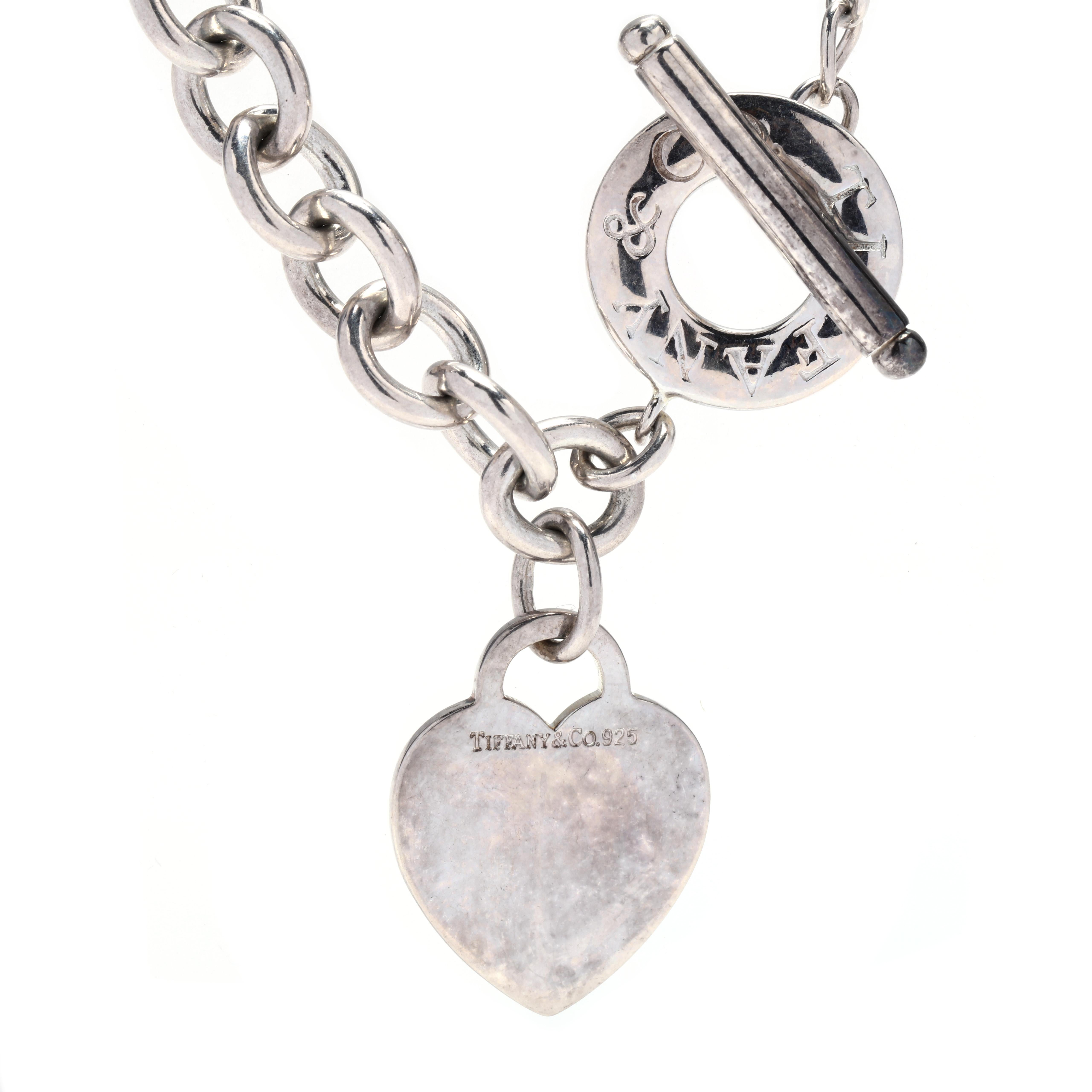 A Tiffany and Company sterling silver heart charm toggle necklace. This necklace features an oval link chain with a flat heart charm and a toggle clasp that is stamped Tiffany & Co.



Length: 16 in.



Width: 9.8 mm



Charm Length: 1.25