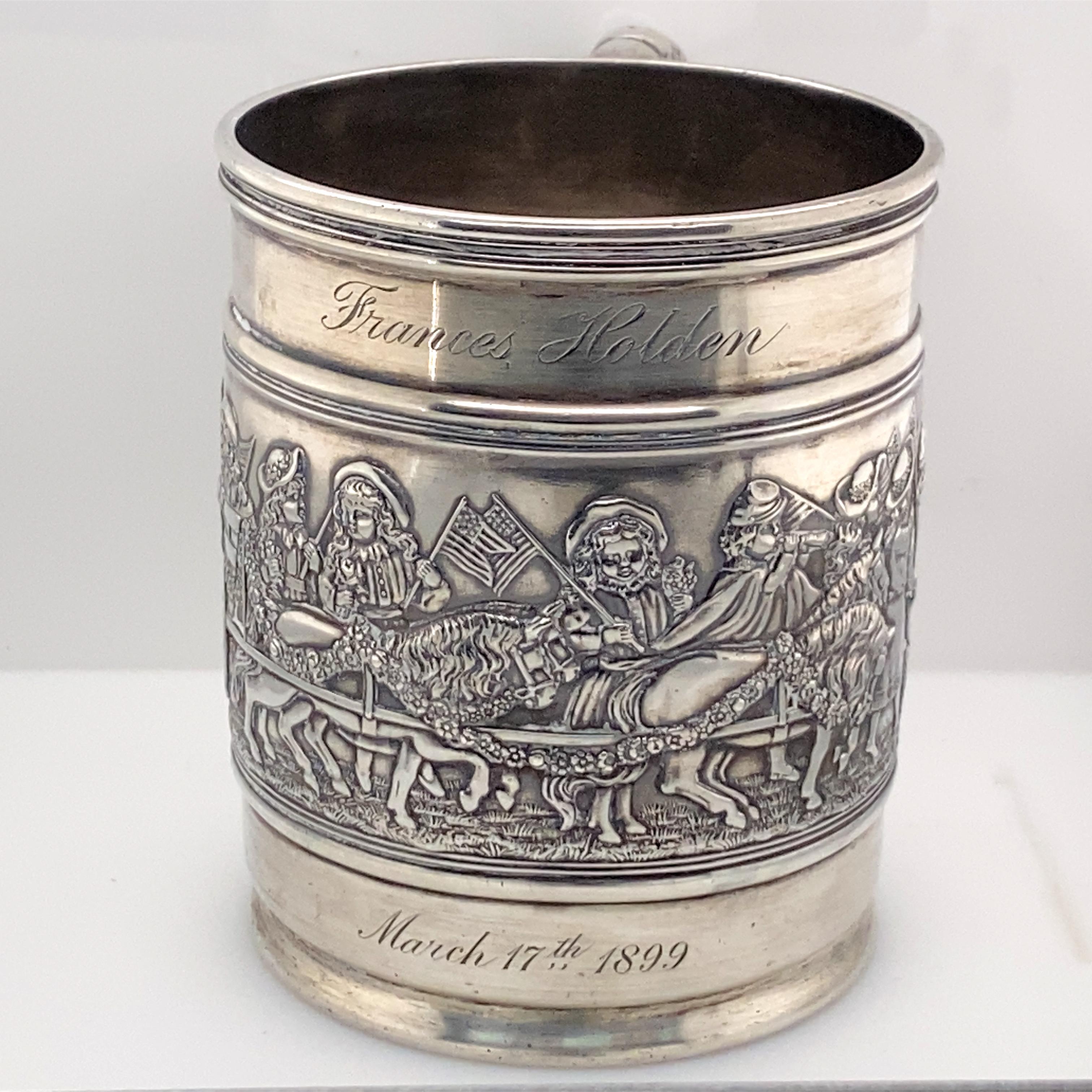 Tiffany & Co. sterling silver child's cup with patriotic parade scene. 1899. Embossed children waving flags, riding in horse-drawn wagon, and some wearing Civil War uniforms. Ribbed handle with dent. Worn marks for Tiffany & Co. to underside.