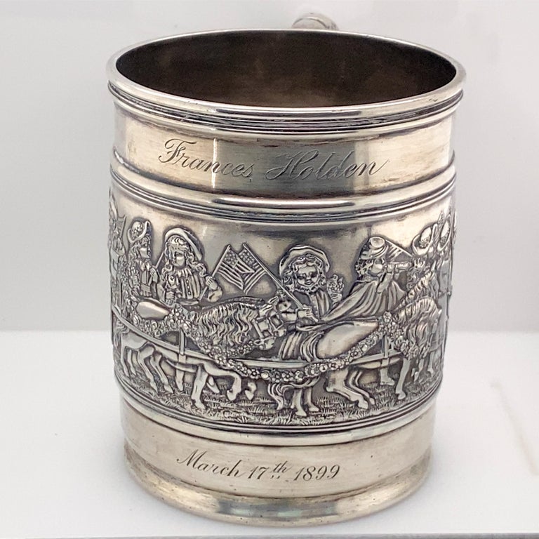 Tiffany & Co. sterling silver child's cup with patriotic parade scene. 1899. Embossed children waving flags, riding in horse-drawn wagon, and some wearing Civil War uniforms. Ribbed handle with dent. Worn marks for Tiffany & Co. to underside.