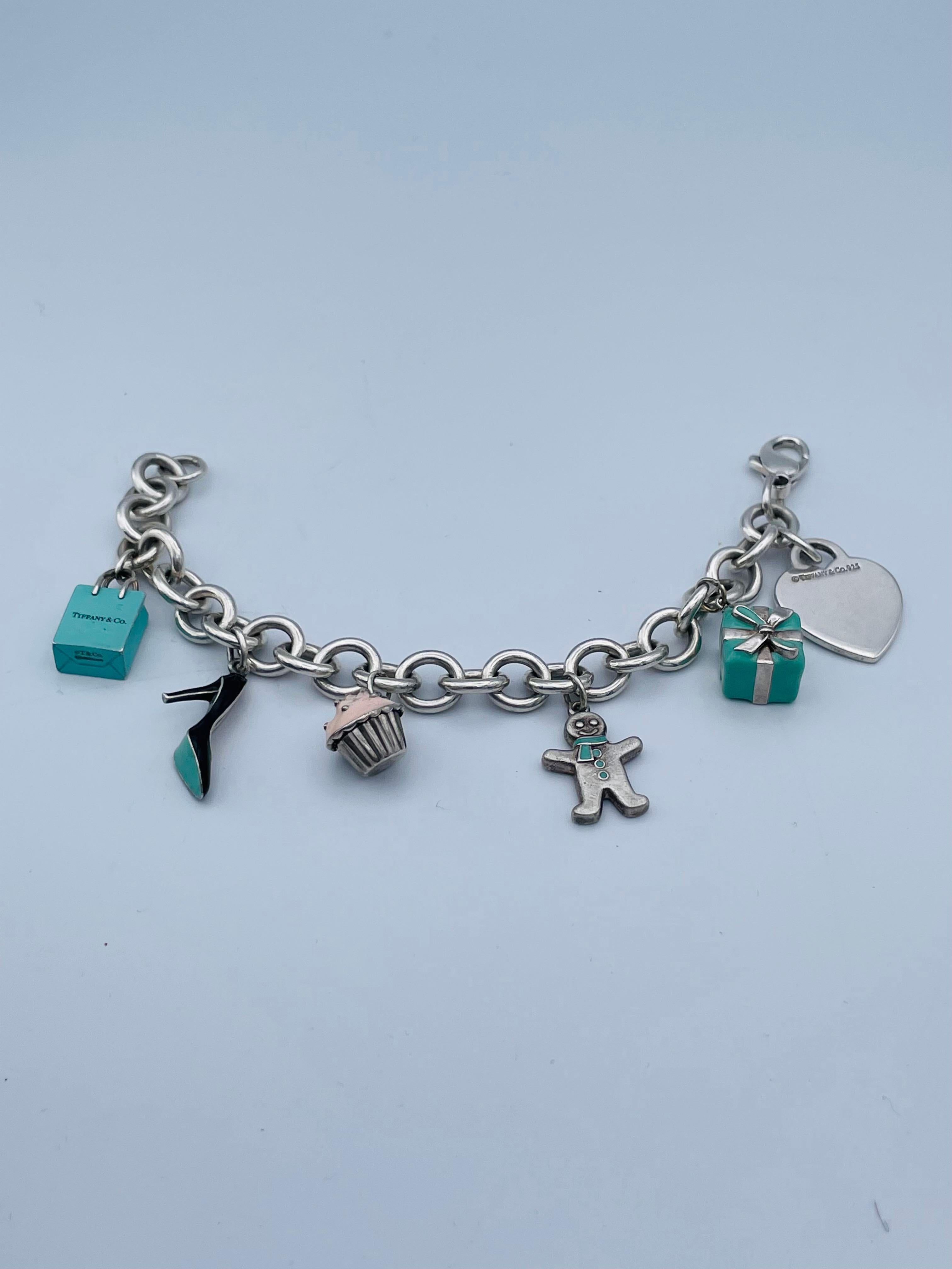 Charming charm bracelet.  Made and signed by TIFFANY & CO.  Sterling silver bracelet, with a sterling heart charm and five enamel figural charms:  a Tiffany bag, a Tiffany box, a cupcake, a high-heeled shoe and a gingerbread man. . 7