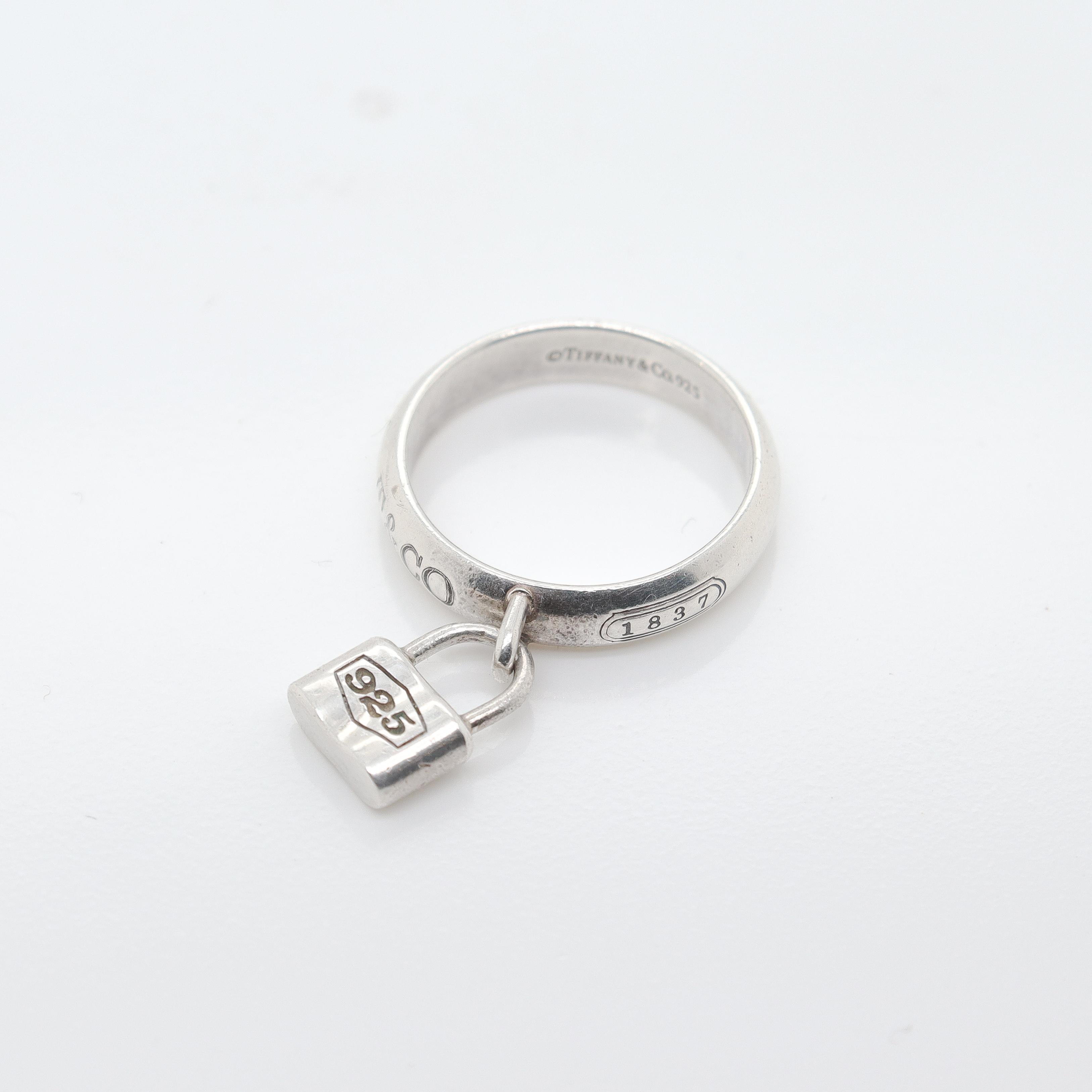 A fine Tiffany & Co. lock charm band ring.

In sterling silver.

Comprised of a round band ring set with a bail and a small attached padlock charm. 

Marked 1837 and T&Co. to the exterior of the band.

Simply wonderful design from Tiffany &