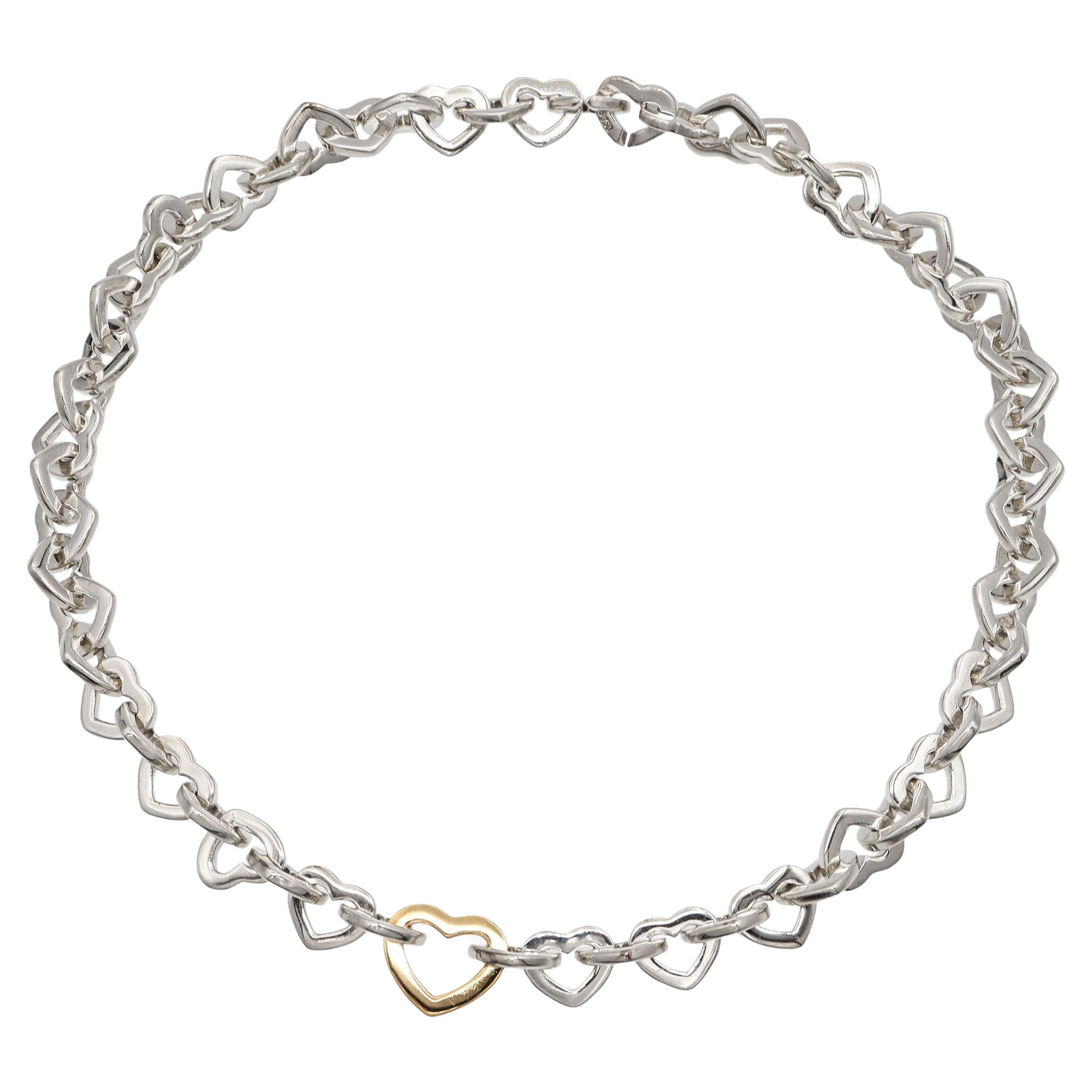 Questa splendida collana di Tiffany & Co. è realizzata con maglie a cuore aperto intrecciate in argento sterling lucido, accentate da un singolo cuore in oro giallo 18 carati per un sorprendente design bicolore. Il pezzo è marchiato 925/750, a