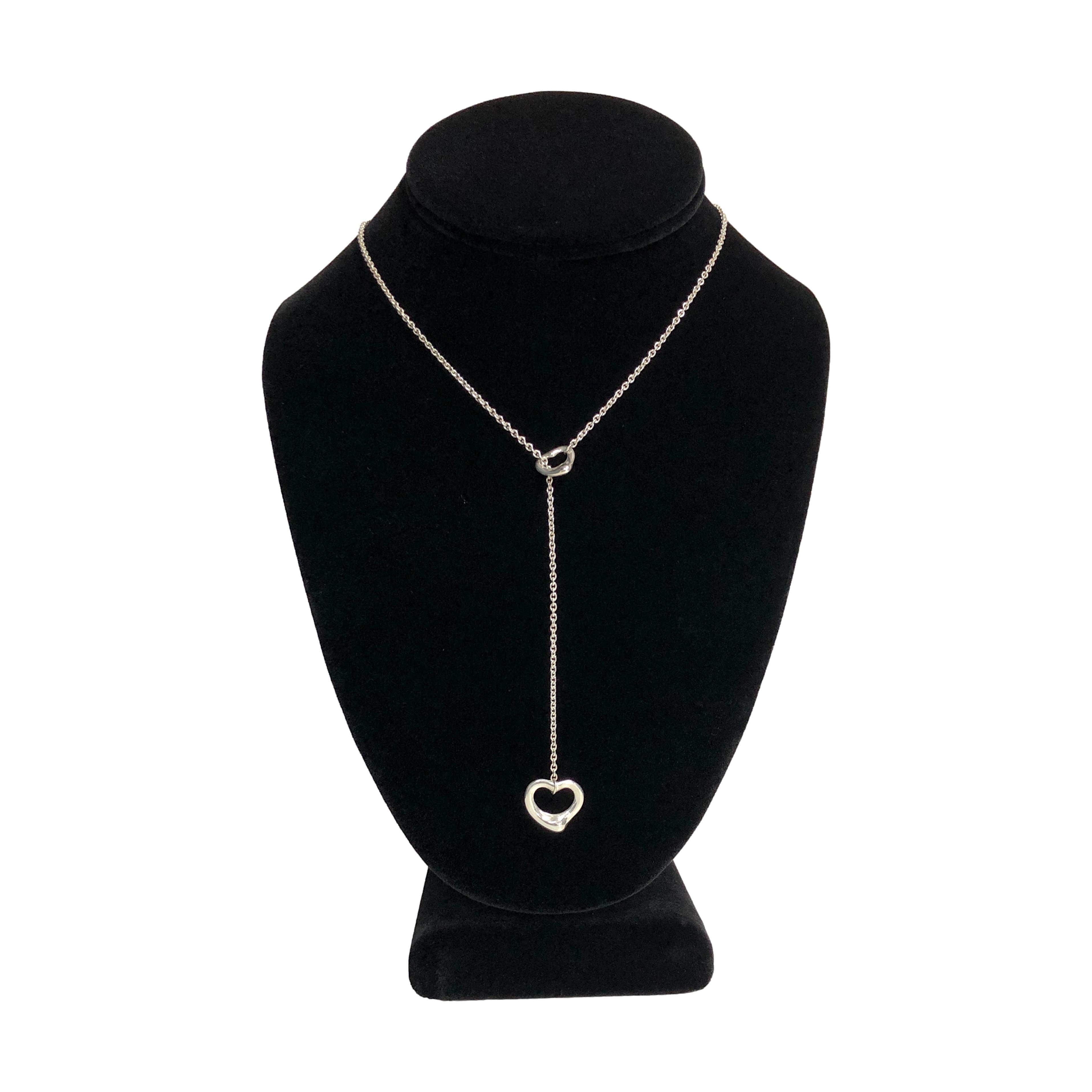 This Tiffany & Co. Open Heart Lariat Necklace, designed by Elsa Peretti, is crafted from sterling silver and features two interlocking open-heart motifs. The larger heart measures 16mm, while the smaller one is 11mm. The lariat-style design allows