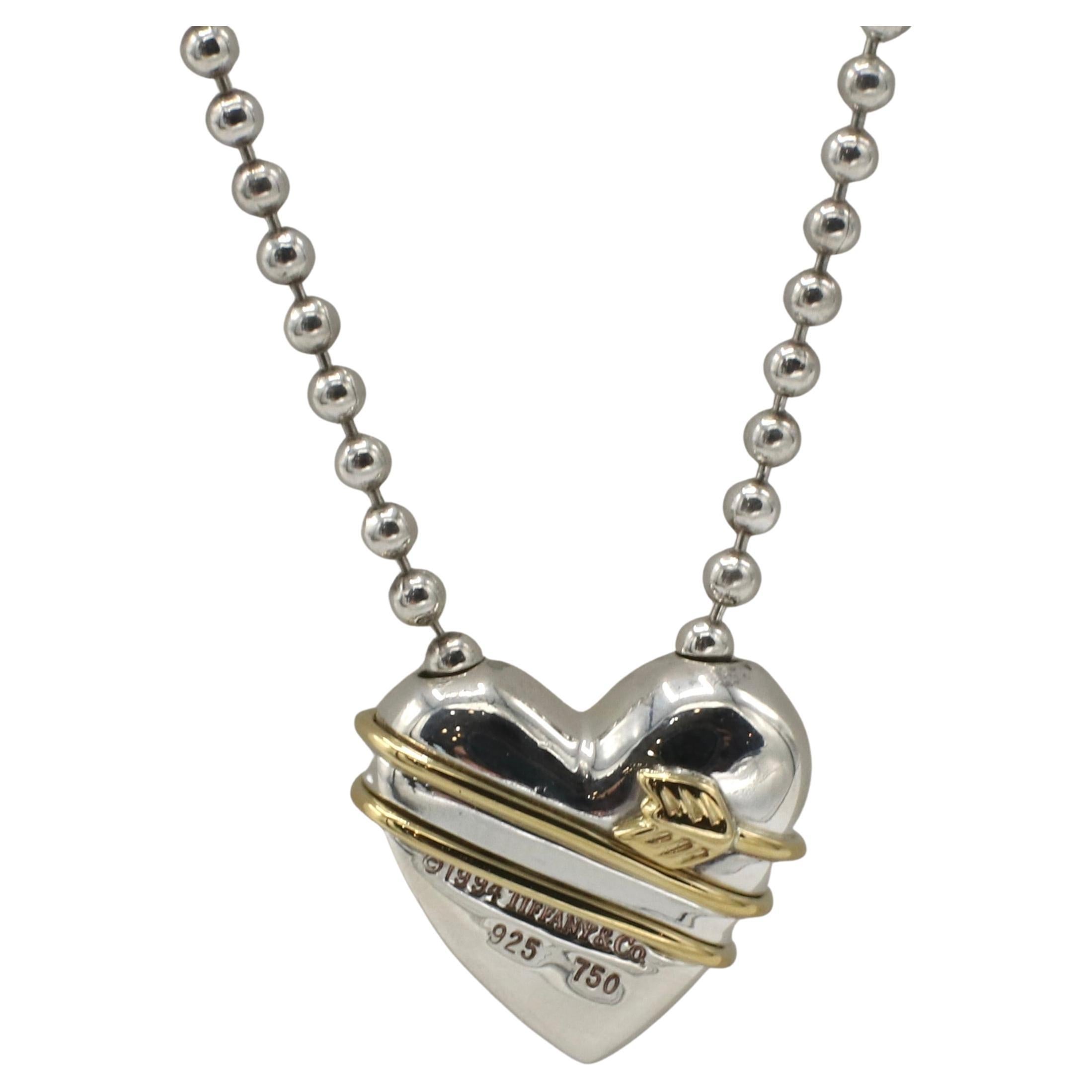 Tiffany & Co. Sterling Silver & Gold Bead Ball Chain Heart Arrow Necklace 
Metal: Sterling silver & 18 karat yellow gold
Weight: 20.15 grams
Heart: 18 x 20mm
Chain: 18 inches
Signed: ©1994 Tiffany & Co. 925 750
SKU: TK I-15378

