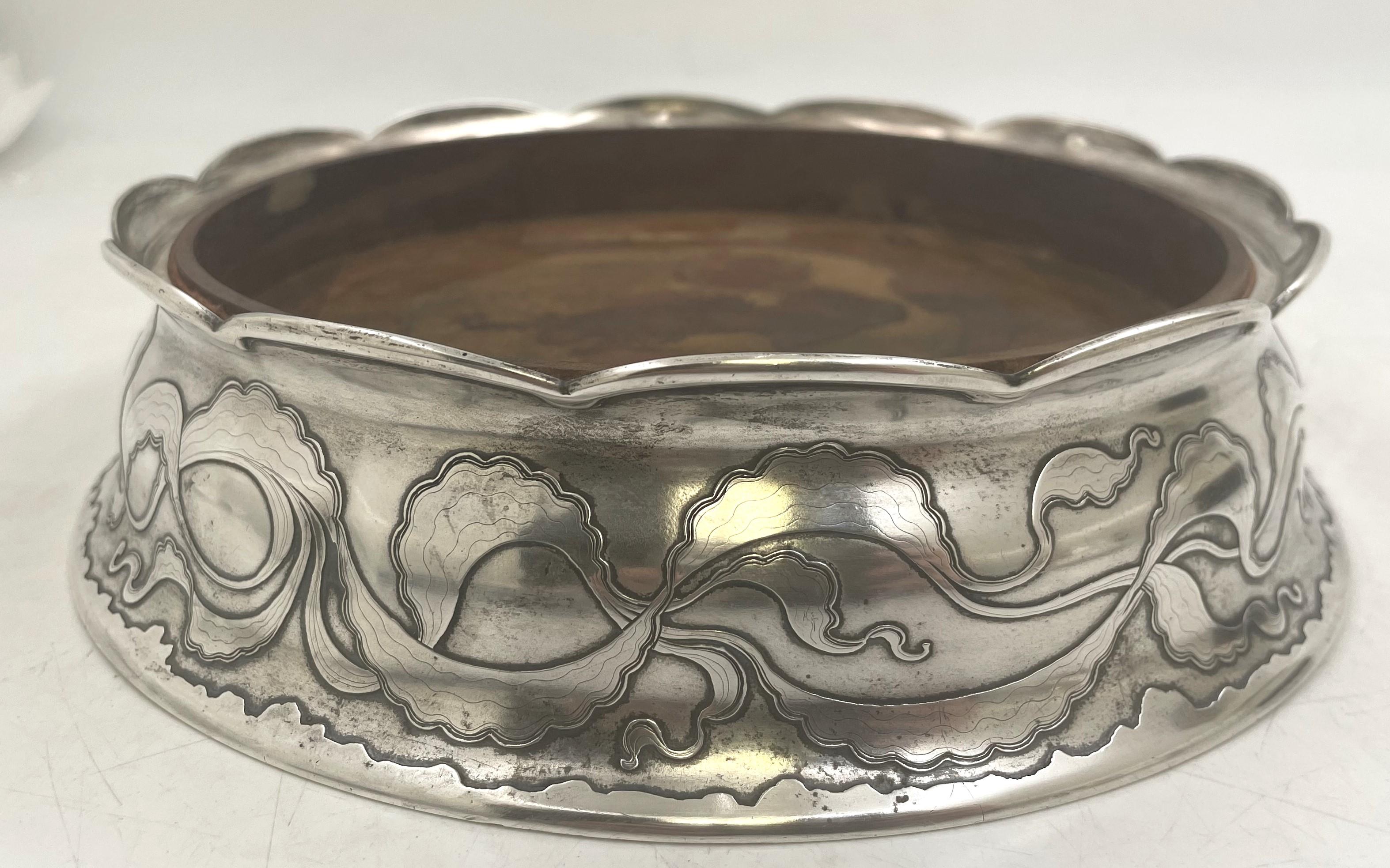 Sottobicchiere per bottiglie magnum in argento sterling di Tiffany & Co. realizzato tra il 1892 e il 1902, con legno al centro, splendidamente decorato con motivi geometrici stilizzati incisi all'acido. Misura 7 1/4'' di diametro in alto (8'' alla