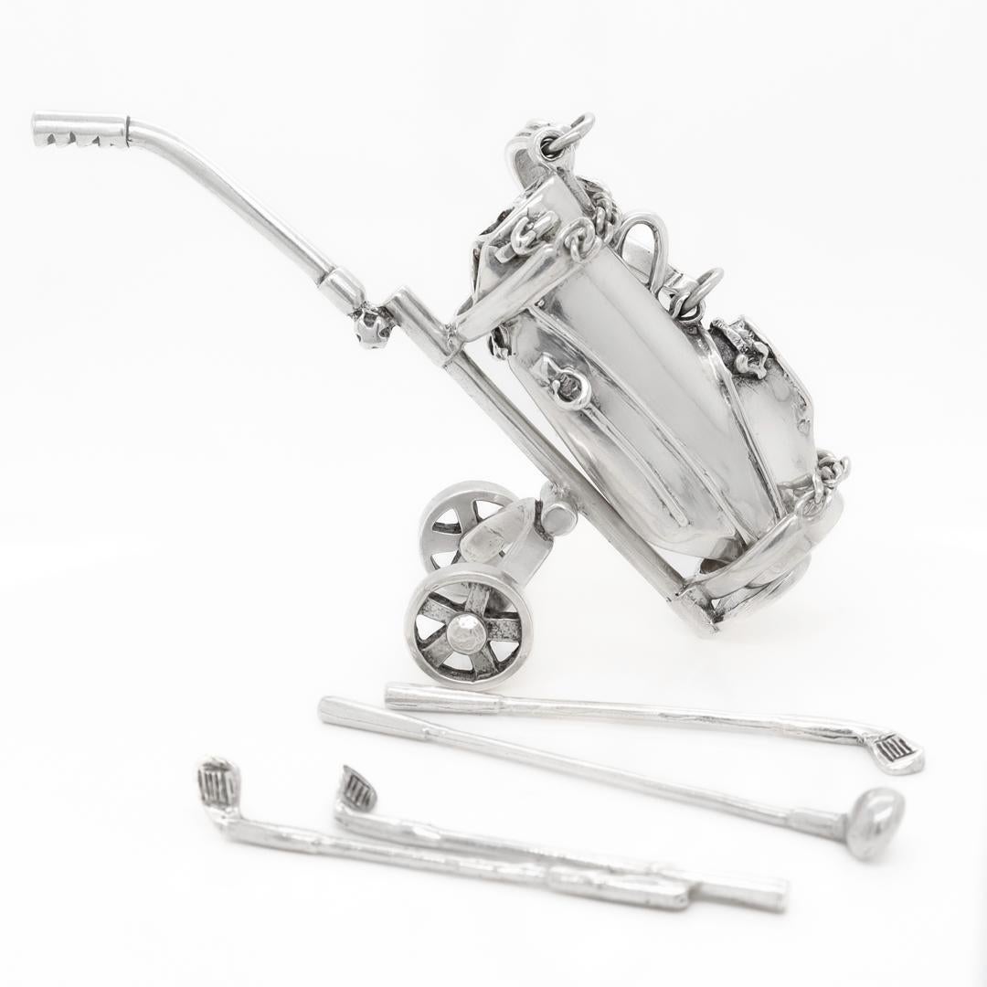 A fine miniature sterling silver golf set.

By Tiffany & Co.

Consisting of golf bag, a caddy with wheels, and four golf clubs (1 iron, 3 iron, 6 iron, and 8 iron).

The caddy has two chains that clip onto the caddy to secure it in place.

Simply a