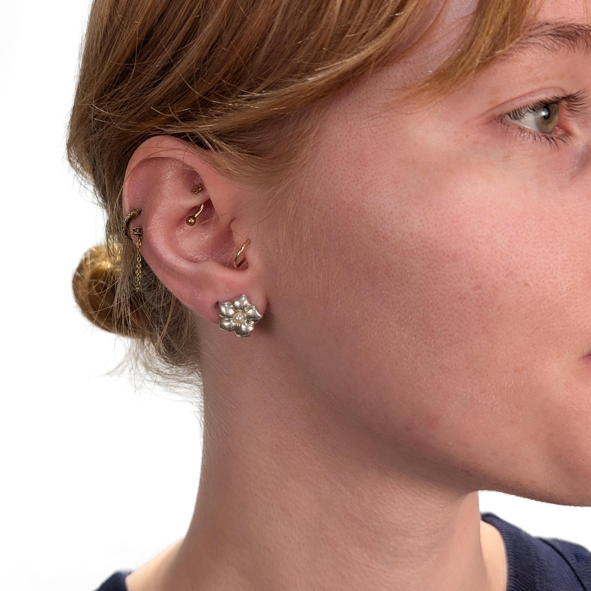 A fine signed pair of silver and pearl earrings.

By Tiffany & Co.

In sterling silver.

Each in the form of a 5 petaled flower with a pearl to its center (reminiscent of a camellia or plumeria flower).

With pushback closures.

Fully marked to the
