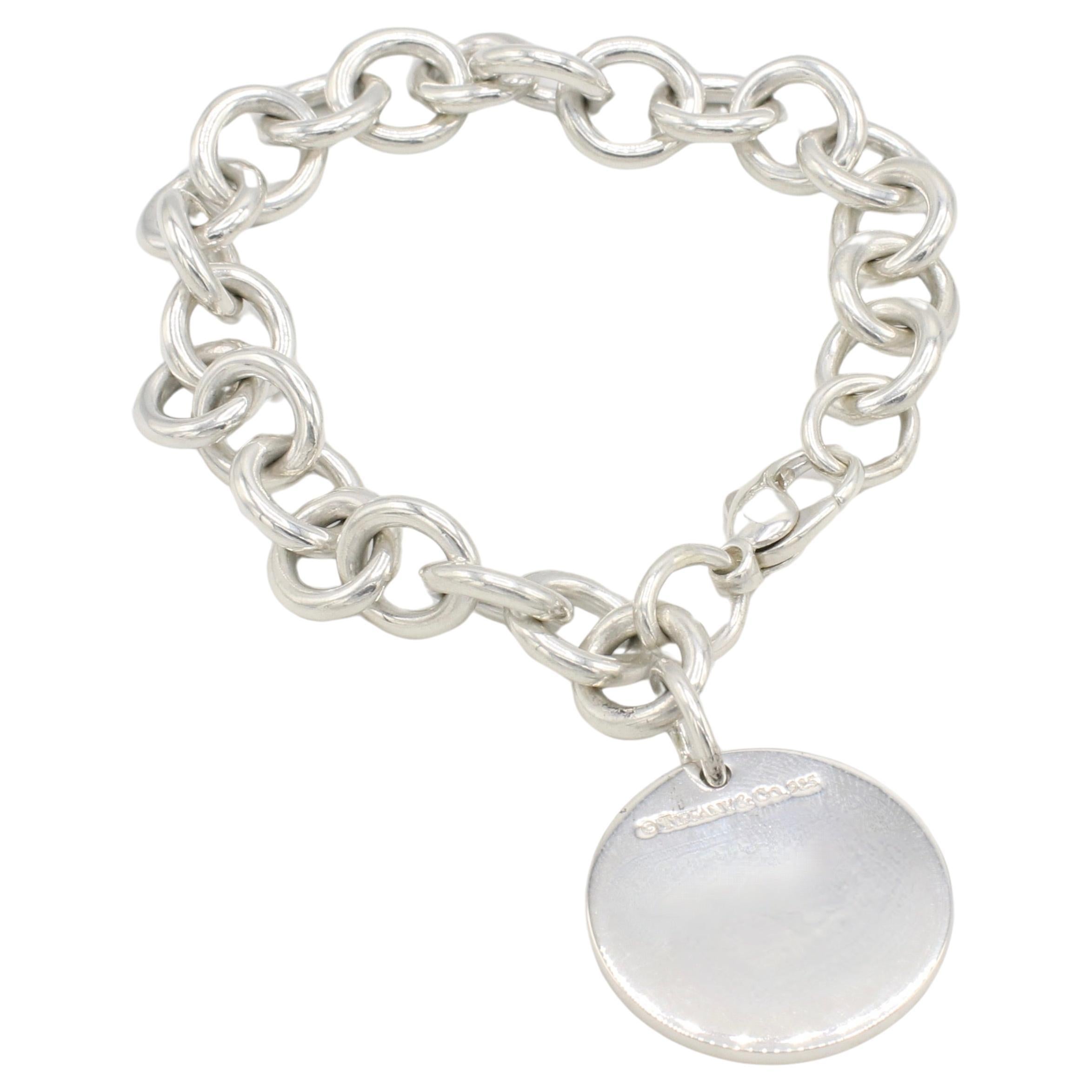 Tiffany & Co. Pulsera de eslabones con charm circular Return To Tiffany de plata de ley 
Metal: Plata de ley
Peso: 33.3 gramos
Longitud: 7 pulgadas
Dije: 24 mm
Firmado: ©Tiffany & Co. 925 Devuélvelo a Tiffany & Co. Nueva York 925
Link: 10 xm