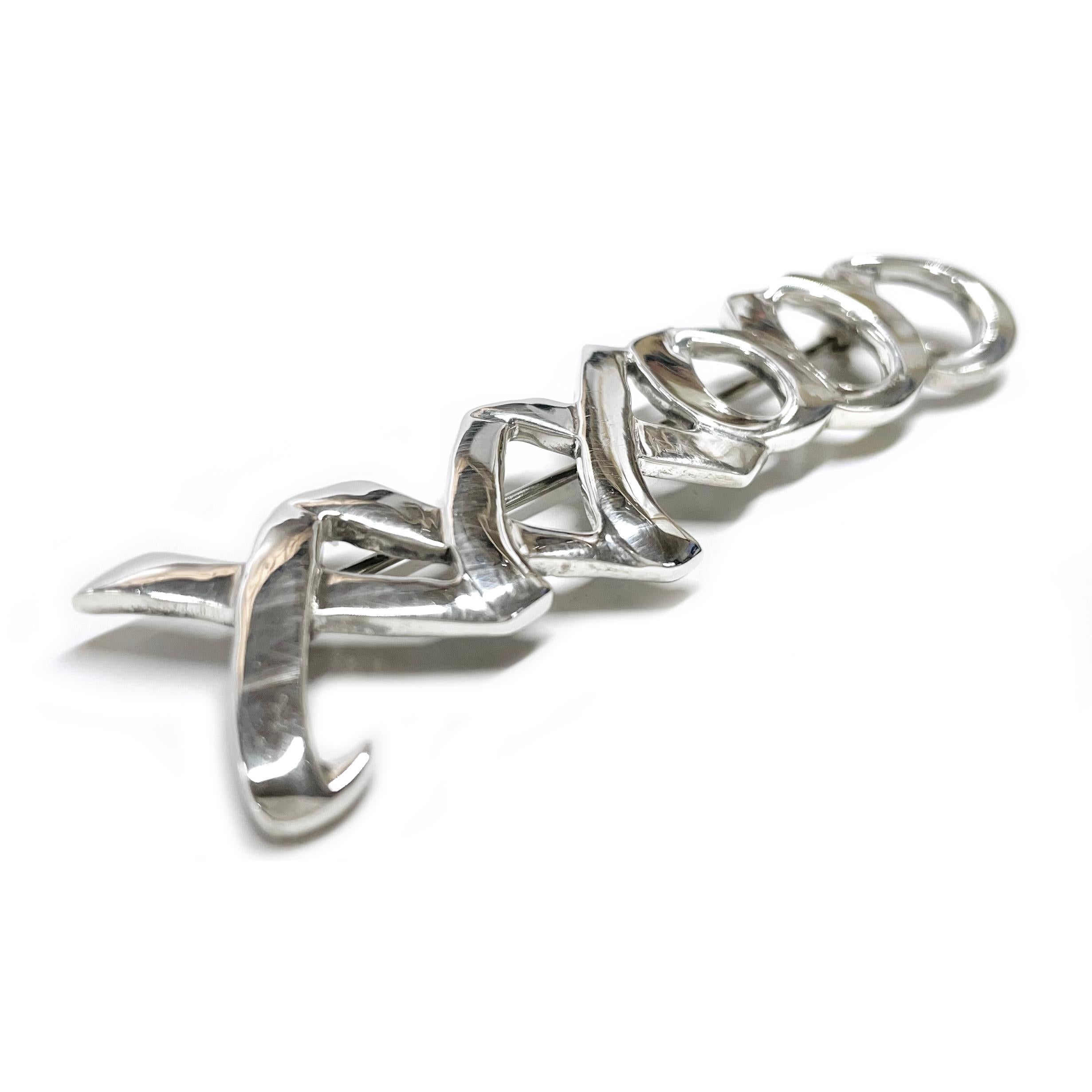 Vintage Tiffany & Co. Sterling Silver XXXOOO Brooch. The brooch features three x's and three o's in one continuous line. There are light surface scuffs but no major scratches. The brooch measures 18.00 in height and 68.62mm in width. Stamped on the