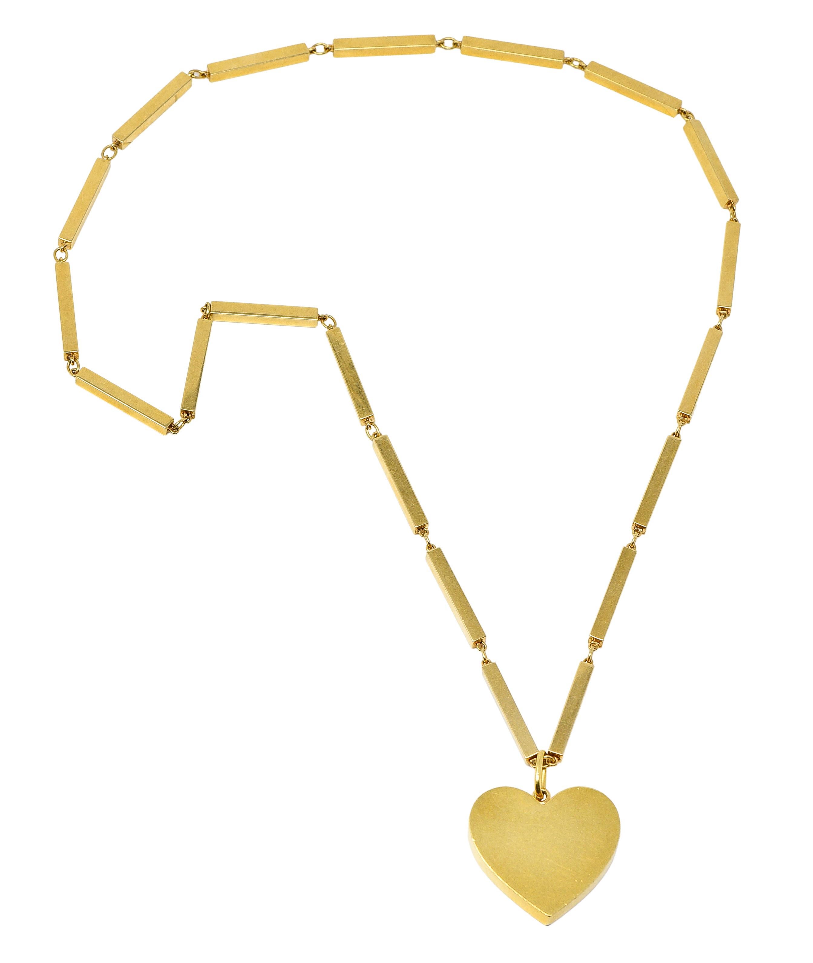 Comprised of a rectangular bar link chain suspending a large heart pendant. Heart is a dimensional flat faced form with a large bale. Featuring a high polish finish. Pendant is stamped for 18 karat gold. Chain is stamped for 14 karat gold. Fully
