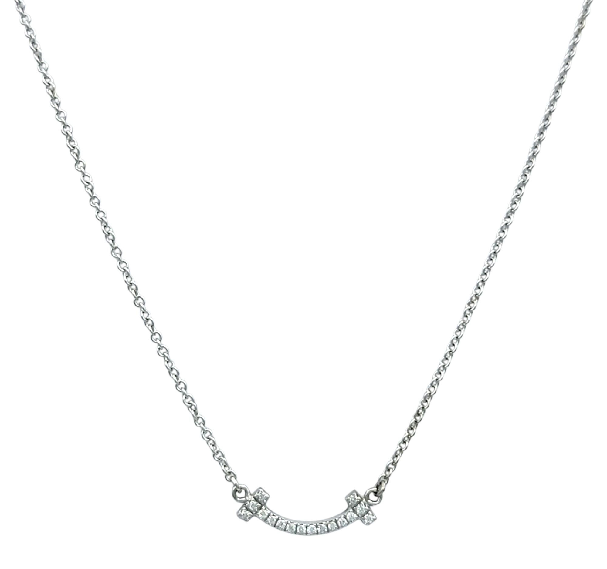 Ce collier authentique de Tiffany & Co. présente le pendentif bien-aimé Tiffany AT&T Smile dans un format mini délicat, serti dans de l'or blanc 18 carats. La barre légèrement incurvée est sertie de seize diamants ronds de taille brillante, ajoutant