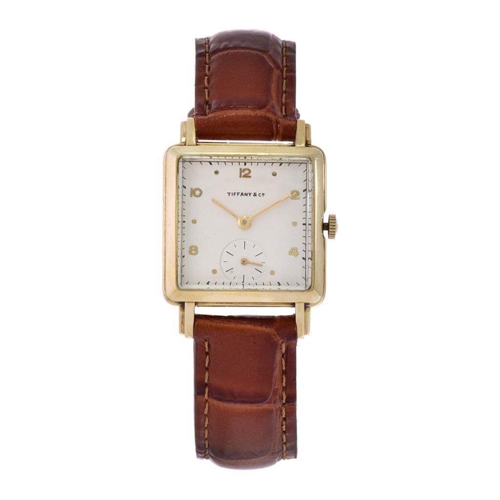Introducing the Tiffany 1950's 14KT Yellow Gold Watch – a vintage gem with a 26x35mm square case. The white dial features gold markers and a sub-dial second hand, exuding classic elegance. Powered by a 17-jewel Movado manual wind movement, this