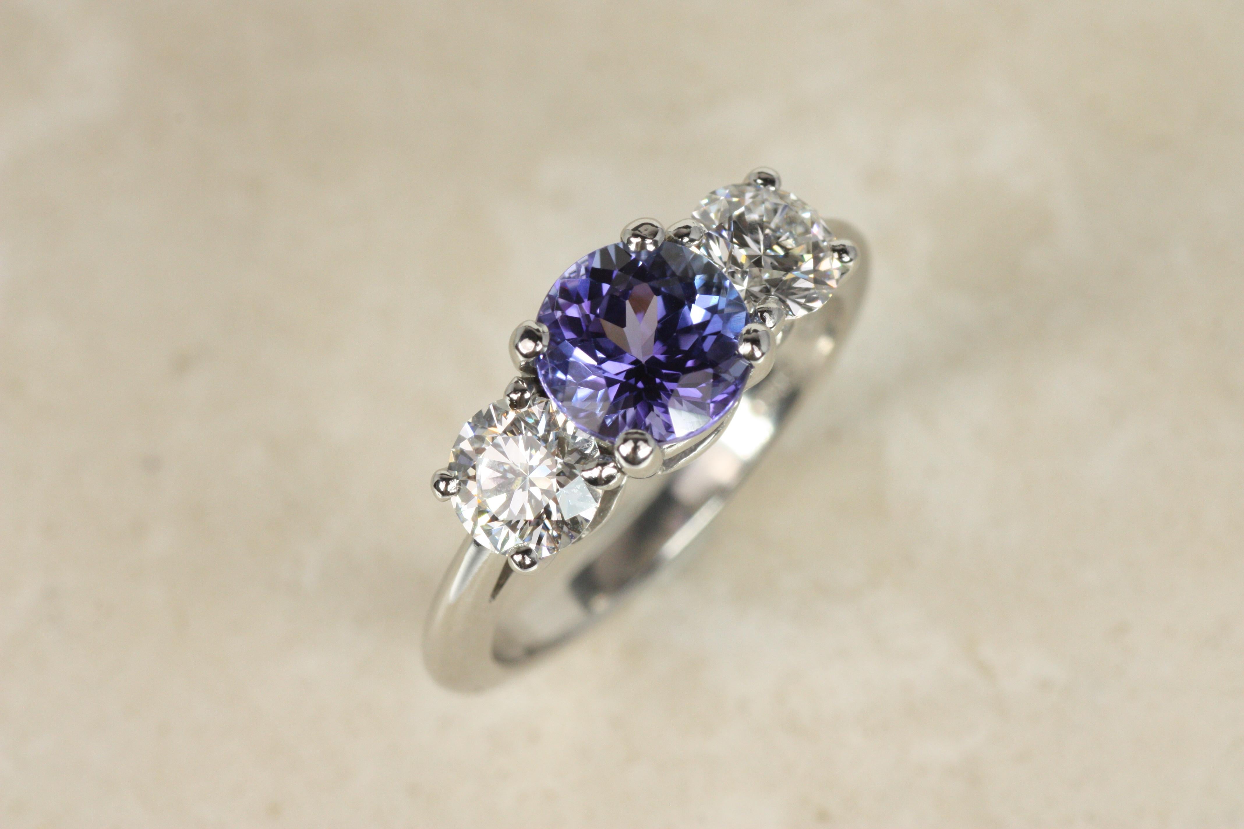 Este anillo de tres piedras de Tiffany & Co., una sofisticada pieza de coleccionista, presenta una fascinante tanzanita de 1,00 ct, enmarcada por dos diamantes naturales redondos de talla brillante (0,80 ctw). Engarzado en platino, este anillo