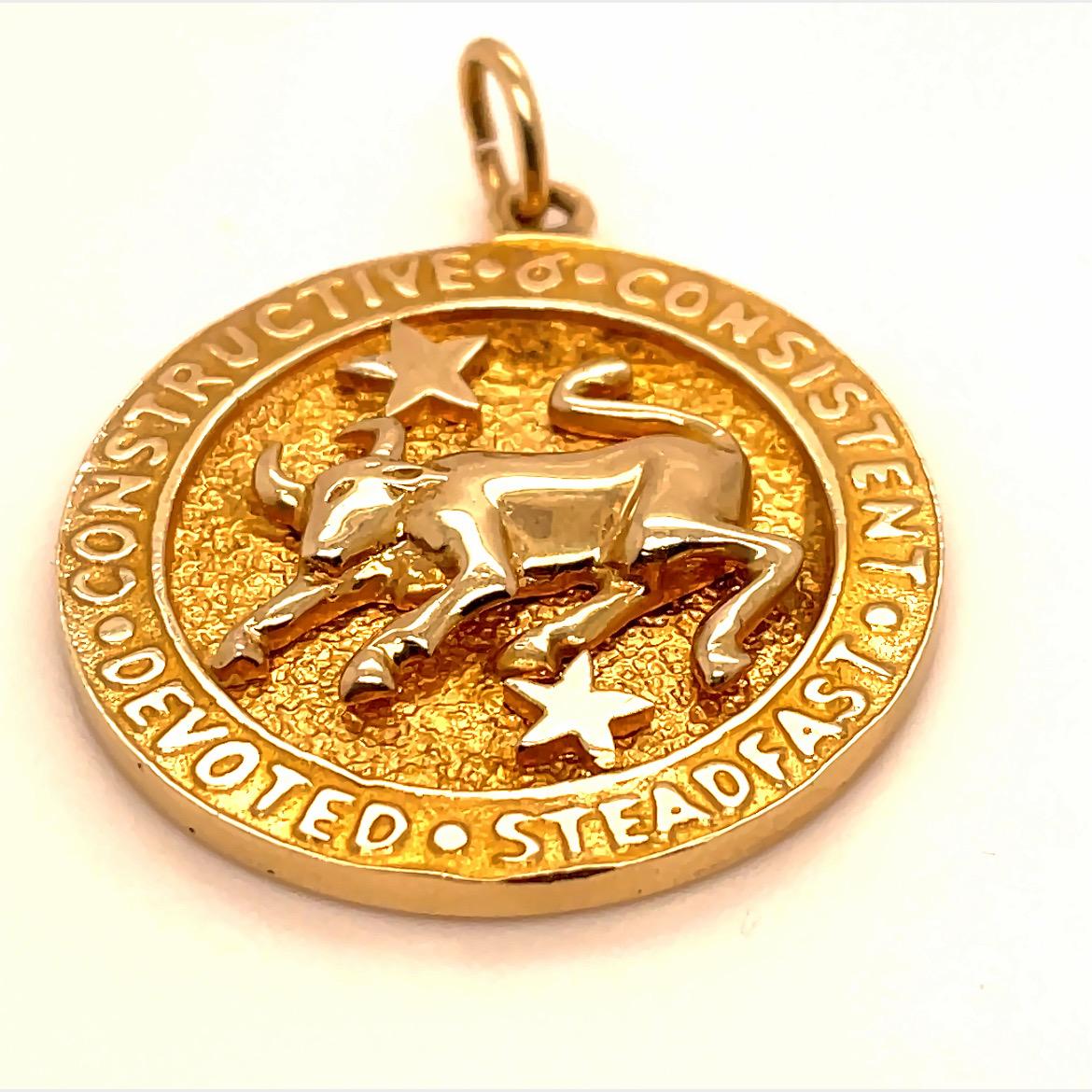 Bold Taurus Zodiac charm/pendant.  Made and signed by TIFFANY & CO.  A three-dimensional bull and two stars in shiny gold are applied to a textured gold background.  Applied letters around the border spell out:  