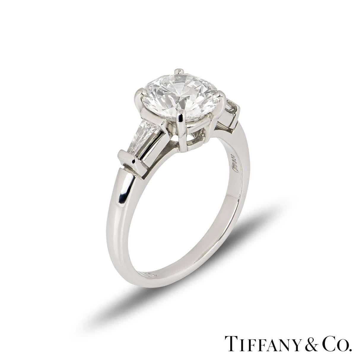 A stunning Tiffany & Co. diamond platinum engagement ring from the Three Stone collection. The ring comprises of a round brilliant cut diamond in a 4 claw setting weighing 2.10ct, E colour and VS1 clarity. Flanked by two tapered baguette cut
