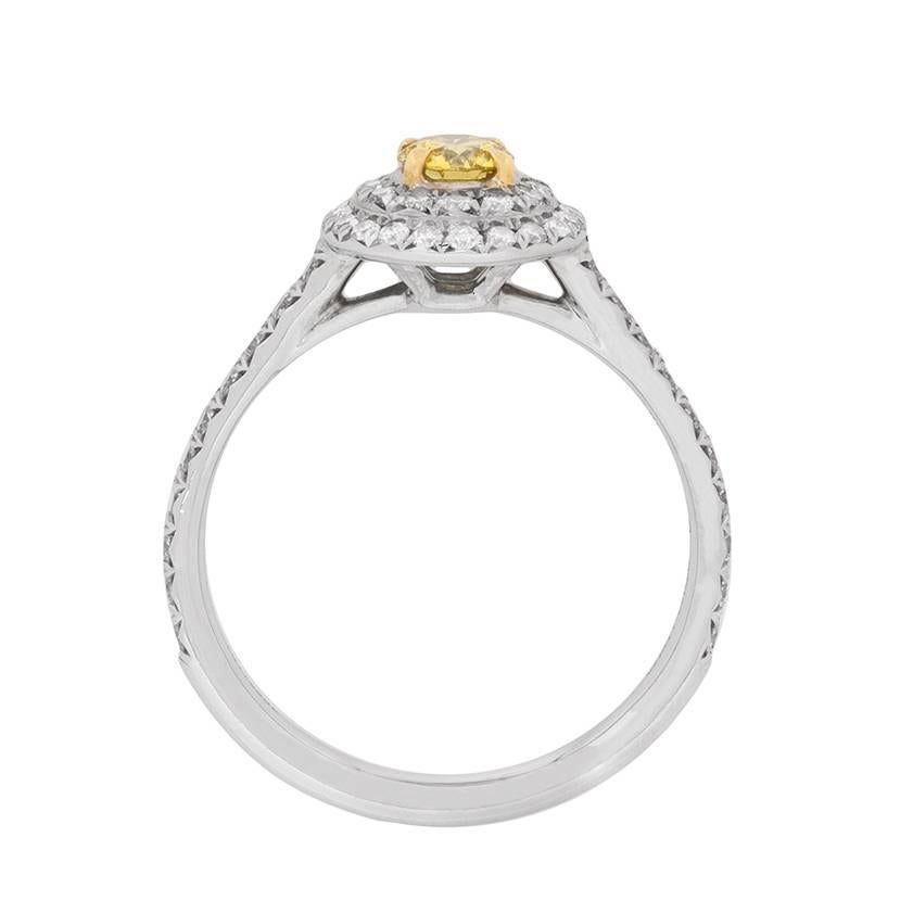A modern Tiffany & Co. classic, this distinctive ring centres a fancy colour yellow diamond weighing 0.18 carat, within the recognisable 'Tiffany Soleste' grain-set double halo setting. The combined weight of the diamond halo's and grain set
