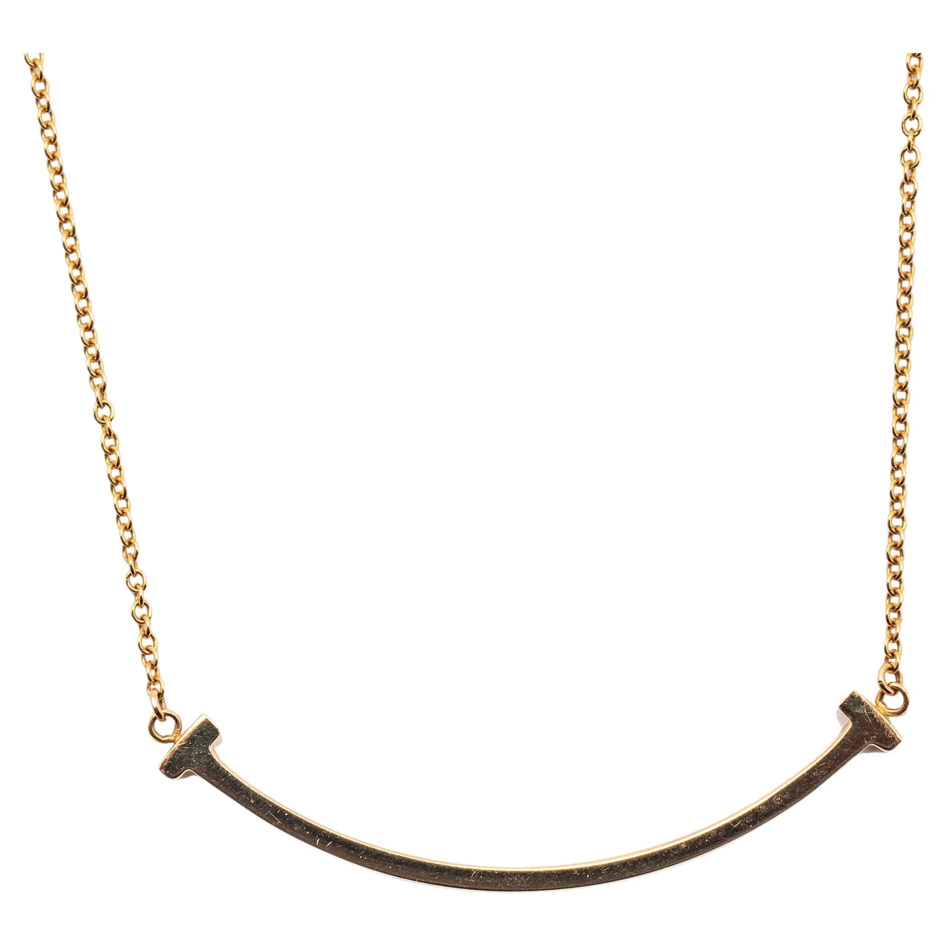 Modern and minimalistic, the beautiful pendant necklace features Tiffany & Co.'s signature Tiffany T letter symbol that resembles strength and resilience. Crafted from 18k rose gold metal, the pendant is shaped like a smile with the letter T on the