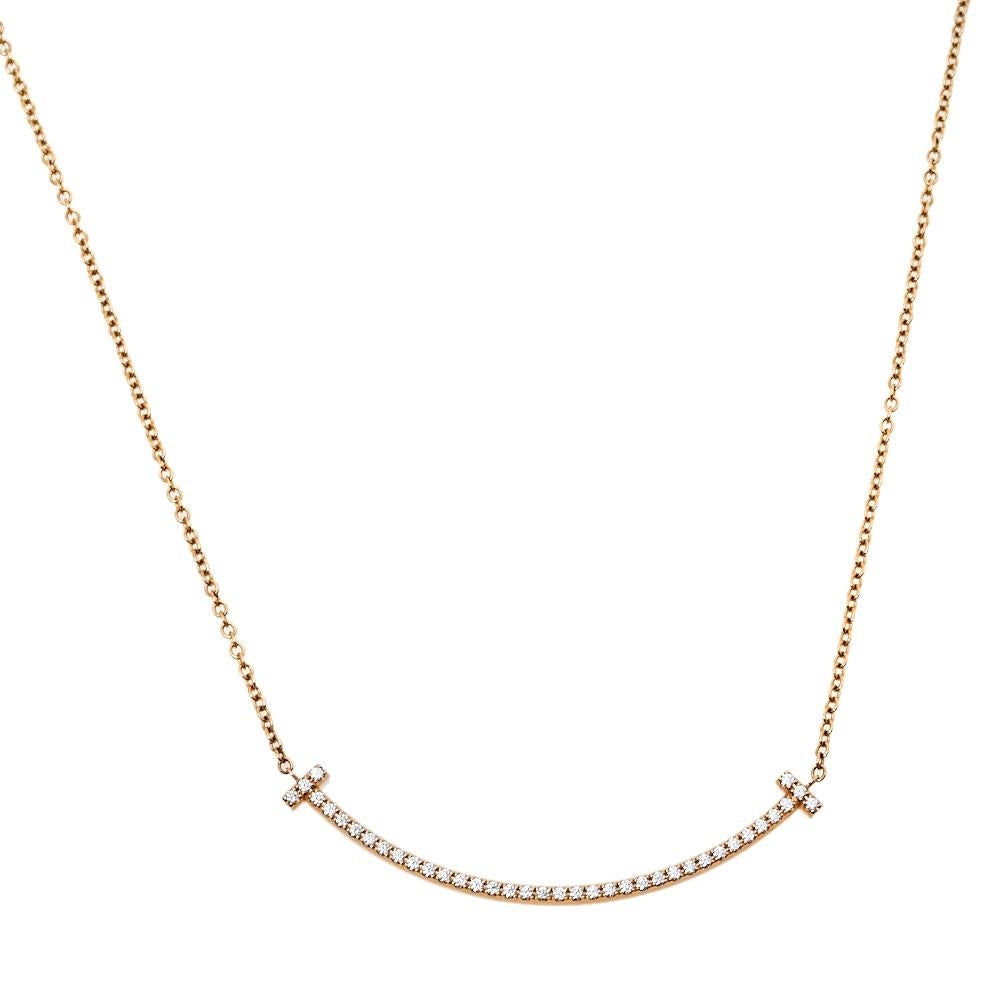 This Tiffany T Smile pendant necklace from Tiffany & Co. is a piece that you will always cherish wearing! Crafted from 18K rose gold metal, it features a slender chain carrying a diamond-embellished T bar pendant that is shaped to resemble a smile.
