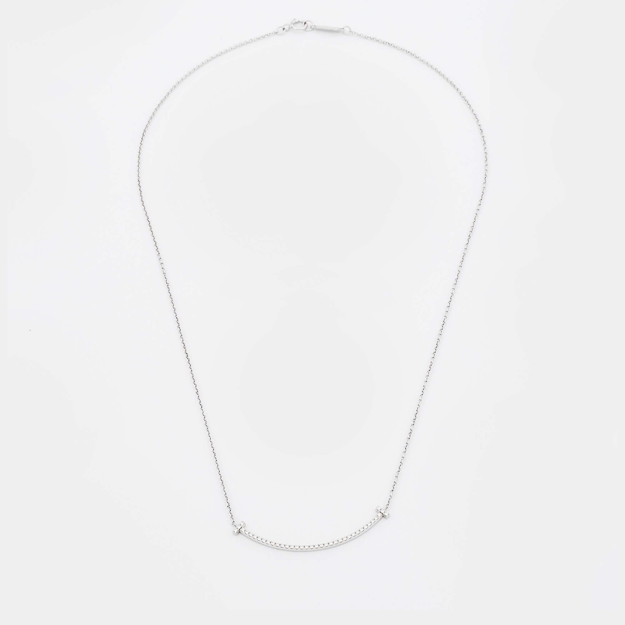 This Tiffany T Smile pendant necklace from Tiffany & Co. is a piece that you will always cherish wearing! Crafted from 18K white gold, it features a slender chain carrying a diamond-embellished T bar pendant that is shaped to resemble a smile. A