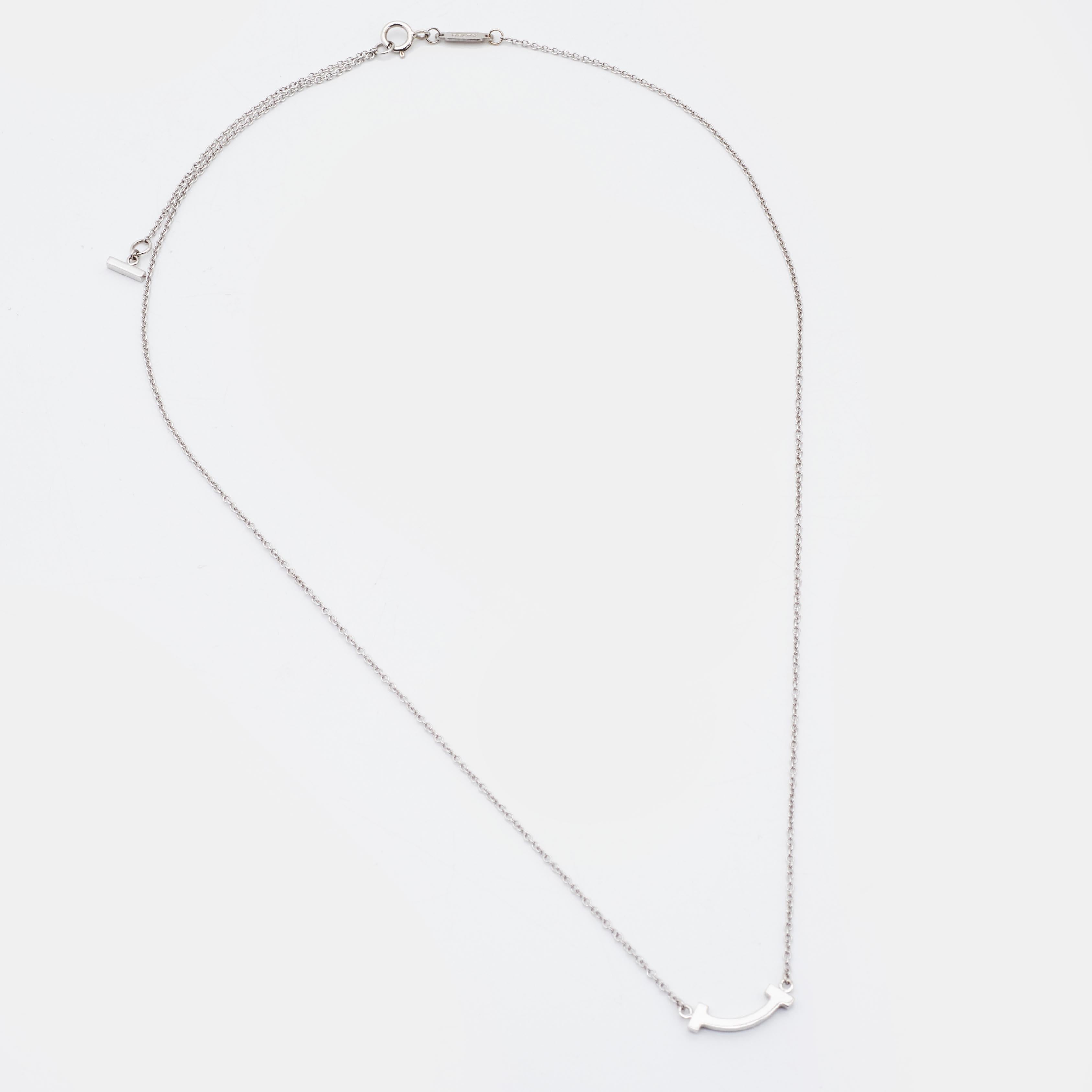 This Tiffany T Smile pendant necklace from Tiffany & Co. is a piece that you will always cherish wearing! Crafted from 18K white gold metal, it features a slender chain carrying a diamond-embellished T bar pendant that is shaped to resemble a smile.