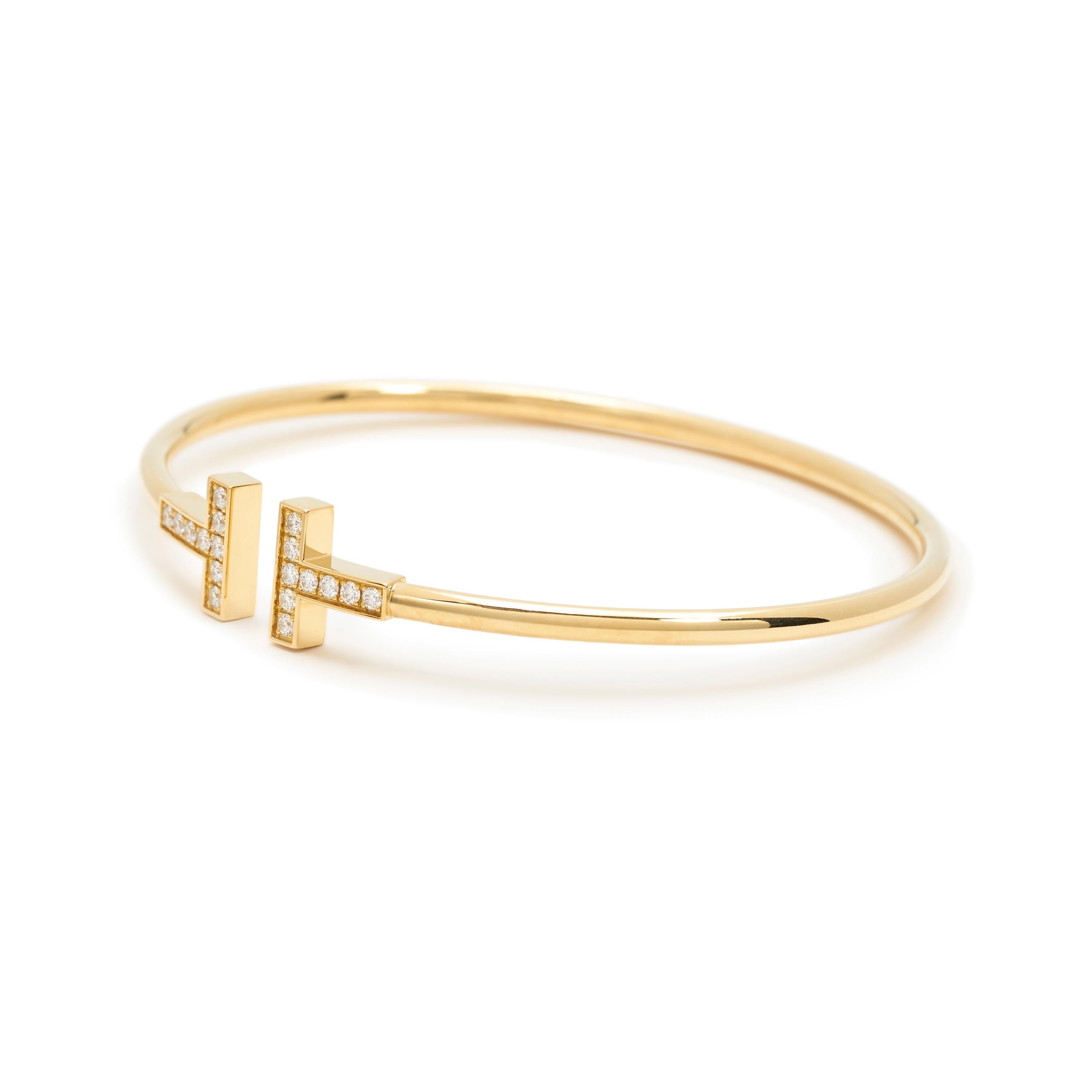 Authentic Tiffany & Co. wire bracelet from the Tiffany T collection crafted in 18 karat yellow gold with 18 diamonds weighing an estimated .22 carats. Size medium, can fit up to a size 6 1/4 wrist. Inspired by the strong, clean lines of the letter
