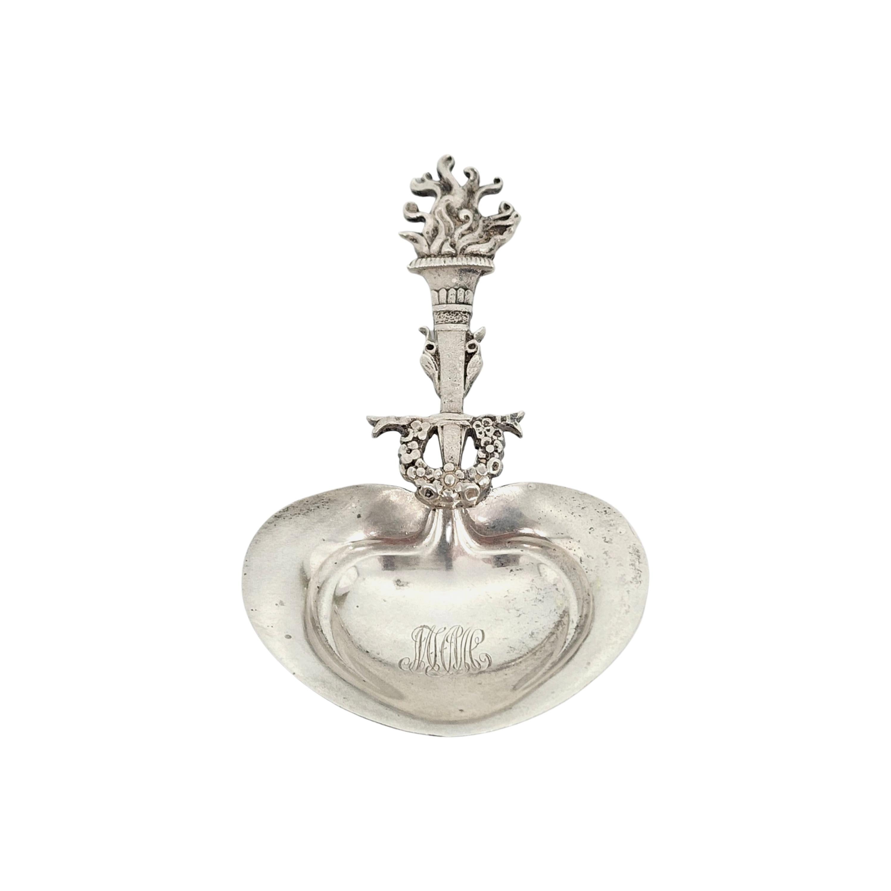 Sterling silver bon bon spoon by Tiffany & Co in a torch and wreath pattern with monogram

Monogram appears to be MFMC

Beautiful and ornate torch handle with a wreath above the bowl. Monogram is intertwined letters in the heart shaped bowl.