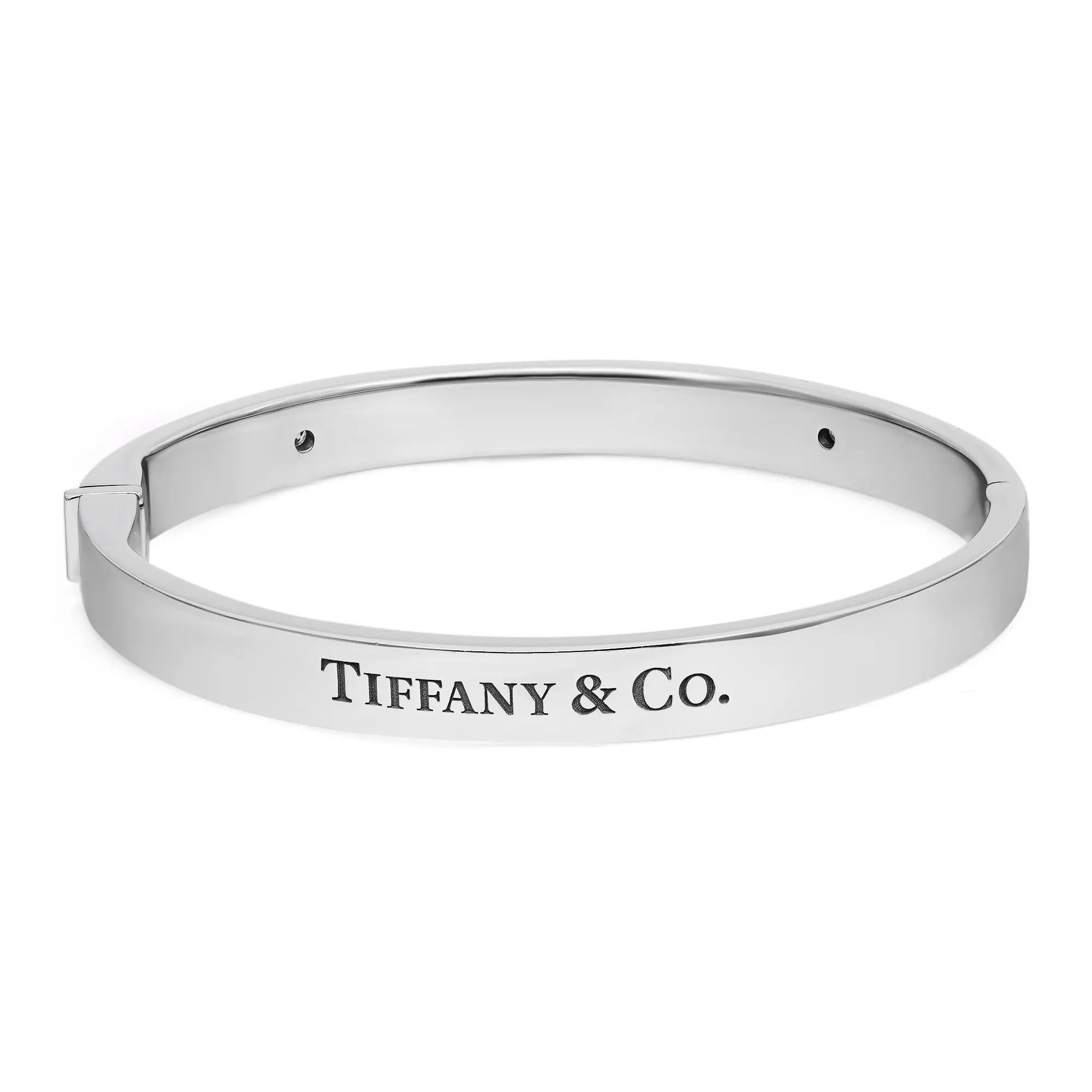 Bold and beautiful, this Tiffany & Co. Two Diamond Logo Hinged Bangle Bracelet is a true essence of jewelry aesthetics. Crafted in lustrous 18K white gold. This bracelet features an oval-shaped hinged bangle studded with 2 round brilliant cut