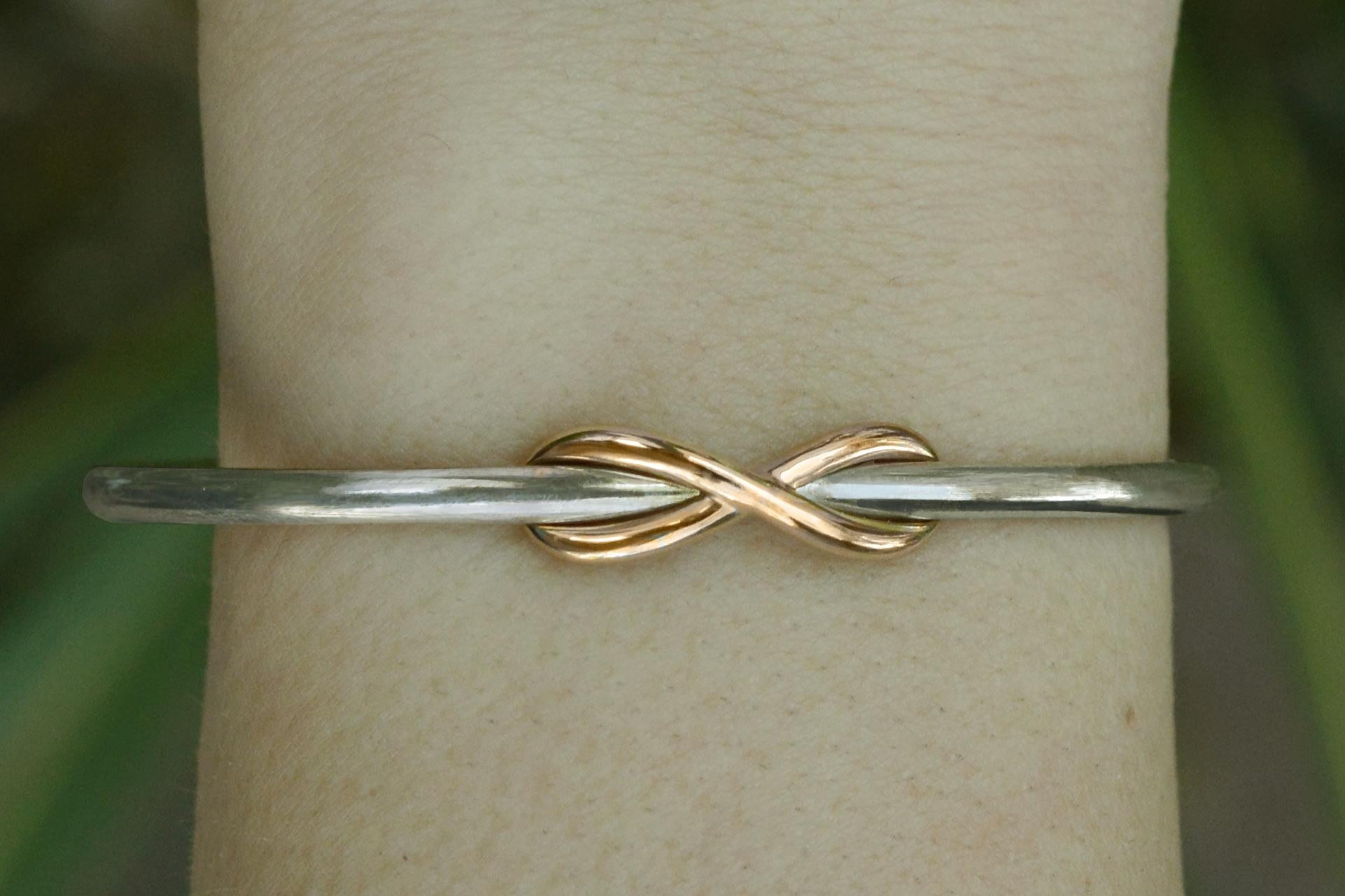 This Tiffany & Co. Infinity bangle bracelet features a sterling silver cuff with a contrasting, intertwined 18k rose gold infinity woven through it. An affordable luxury, this retired, two tone design is no longer available with rose gold. See our