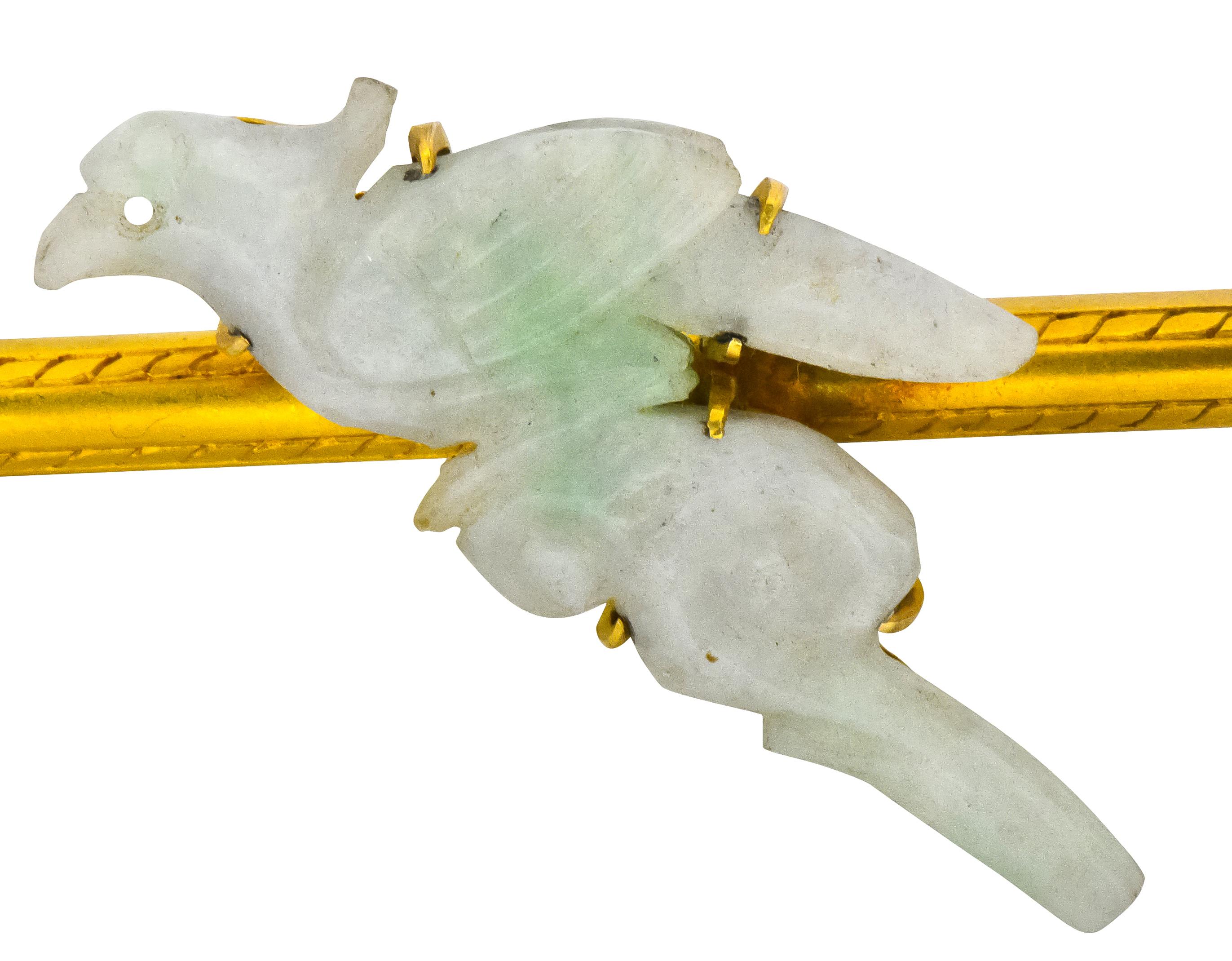 Centering a claw set, carved jade bird on branch, light sage green with mild mottling and good polish

Accompanied by matte, yellow gold bar terminating in domes with striped engraving throughout

Completed by pin-stem and closure

Tested as 18
