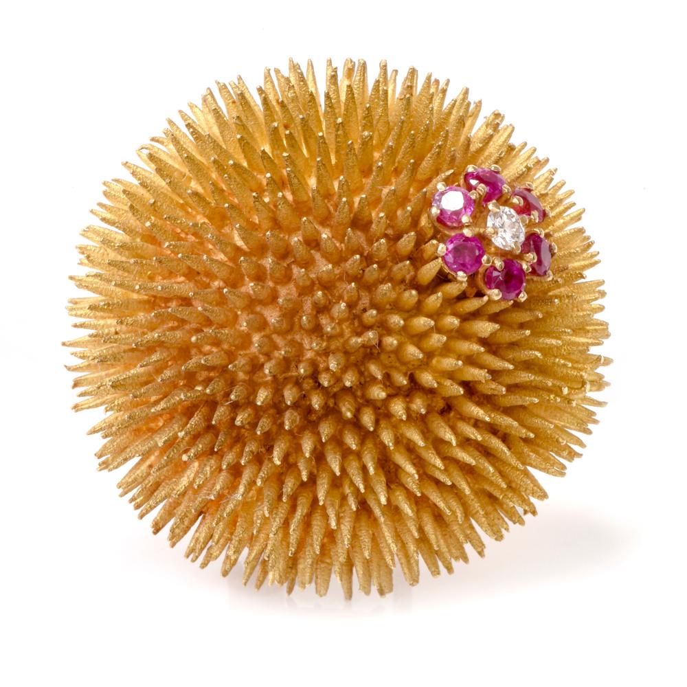 This whimsical pin brooch designed and crafted by Tiffany & Co. simulates the profile of a sea urchin. It is rendered in 18 Karat yellow gold, weighs 43.4 grams and measures 36mm in diameter. It is adorned with 6 round-faceted rubies weighing 0.40