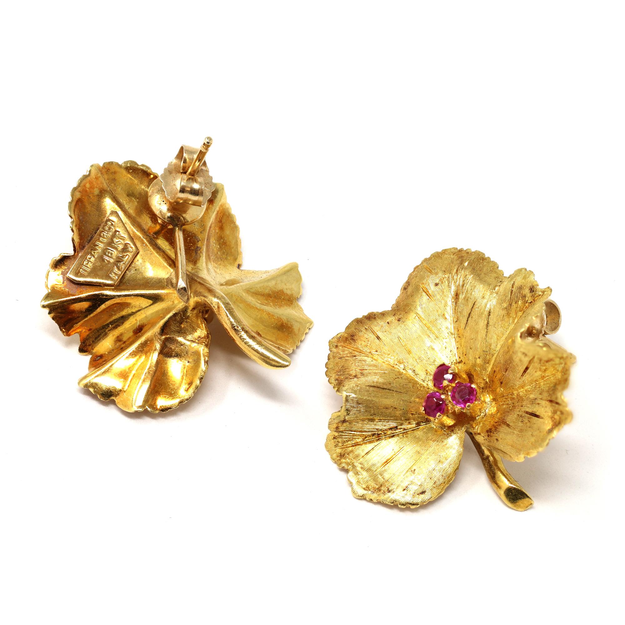 A lovely vintage set of Brooch and earrings signed by Tiffany & Co featuring a leaf motif, each accented with a cluster of Rubies in its center.
The suite is created in 18-karat yellow gold with calibrated natural round rubies presenting a lively
