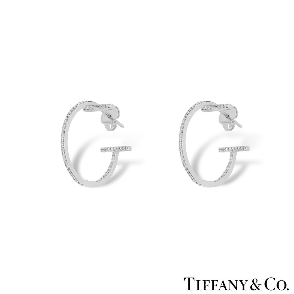 An elegant pair of 18k white gold diamond earrings by Tiffany & Co. from the Tiffany T collection. The earrings are in a hoop style with the iconic Tiffany T motif at the start and finish. The inside out hoops are each pave set with 65 round