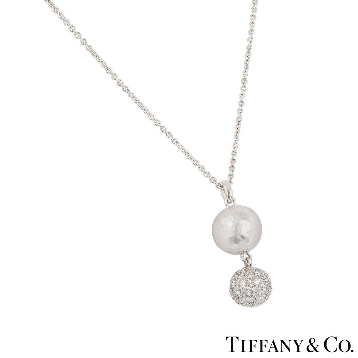 An elegant 18k white gold diamond 2 ball motif by Tiffany & Co. from the Paloma Picasso collection. The necklace features 2 ball motifs, one set with a hammer finish with a smaller ball suspended from it set with pave round brilliant cut diamonds