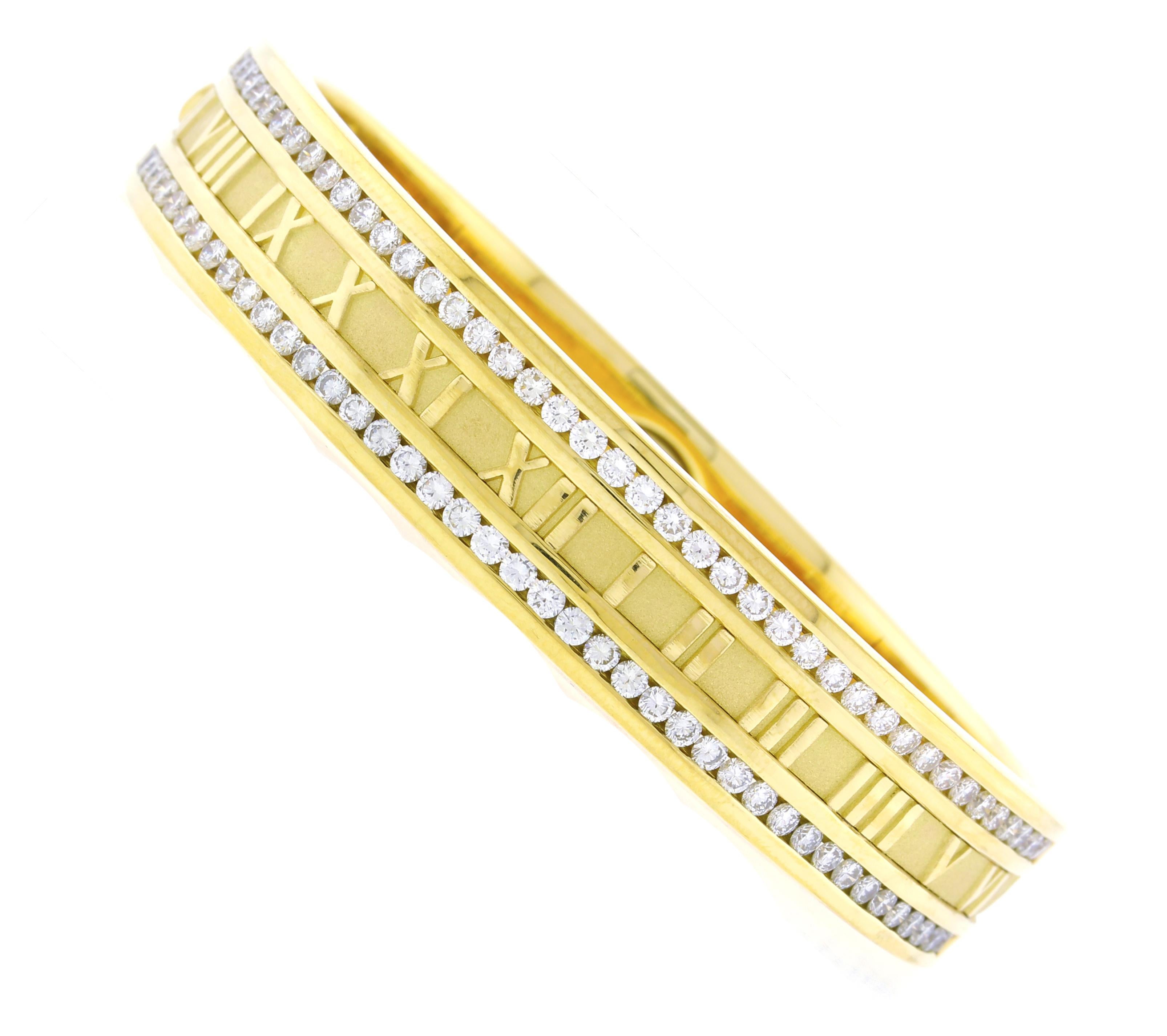 Prova l'eleganza senza tempo e l'eccezionale maestria di questa splendida Tiffany & Co. Bracciale Atlas™ a bracciale largo. Realizzato in ricco oro giallo 18 carati, questo audace pezzo presenta l'iconico motivo del numero romano della rinomata