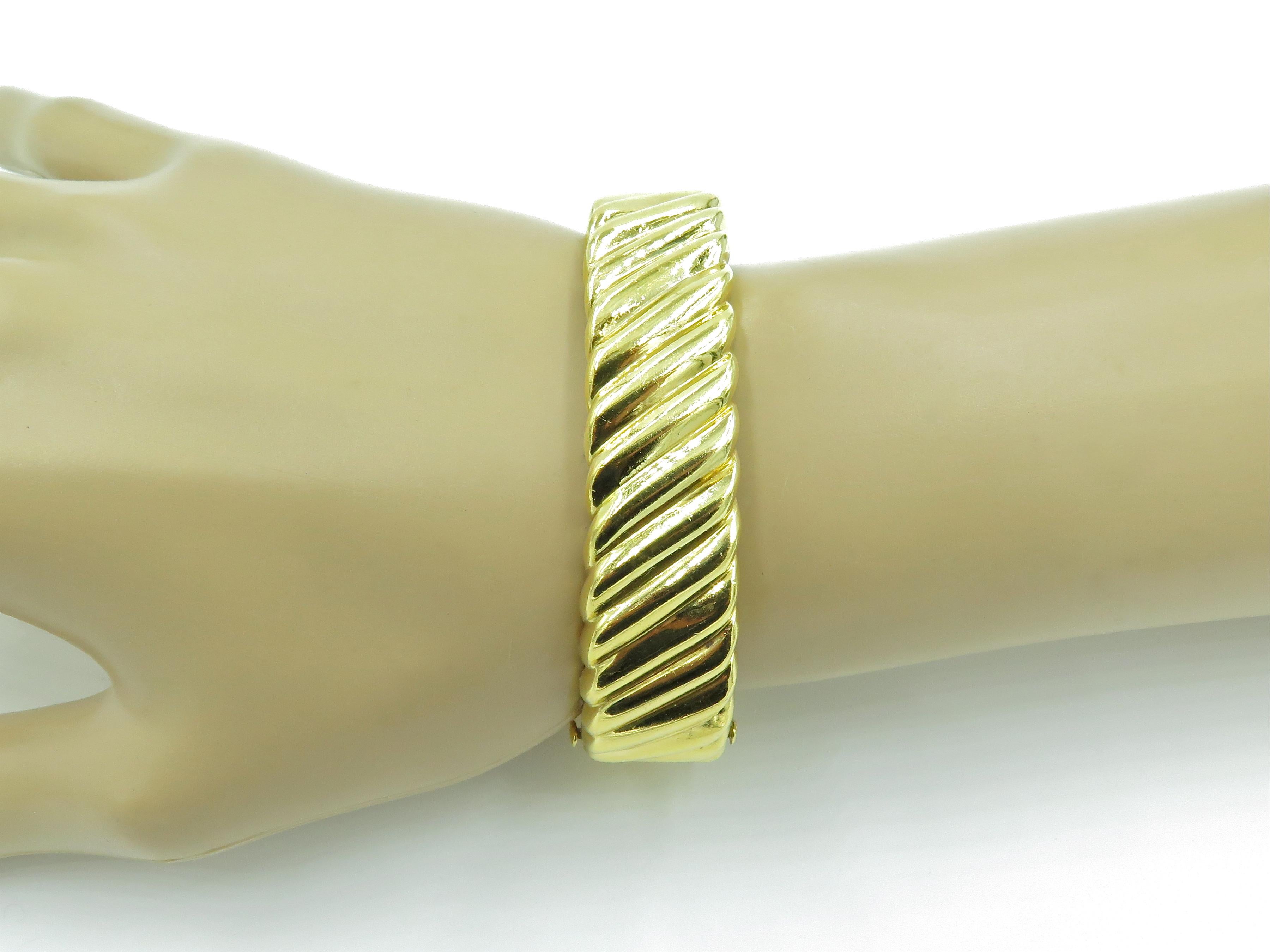 An 18 karat yellow gold bracelet. Tiffany & Co. Circa 1980. The hinged oval shaped bangle of fluted design. Width is approximately 5/8 inch, inside measurement is approximately 6 3/4 inches, diameter is approximately 2 1/4 inches. 