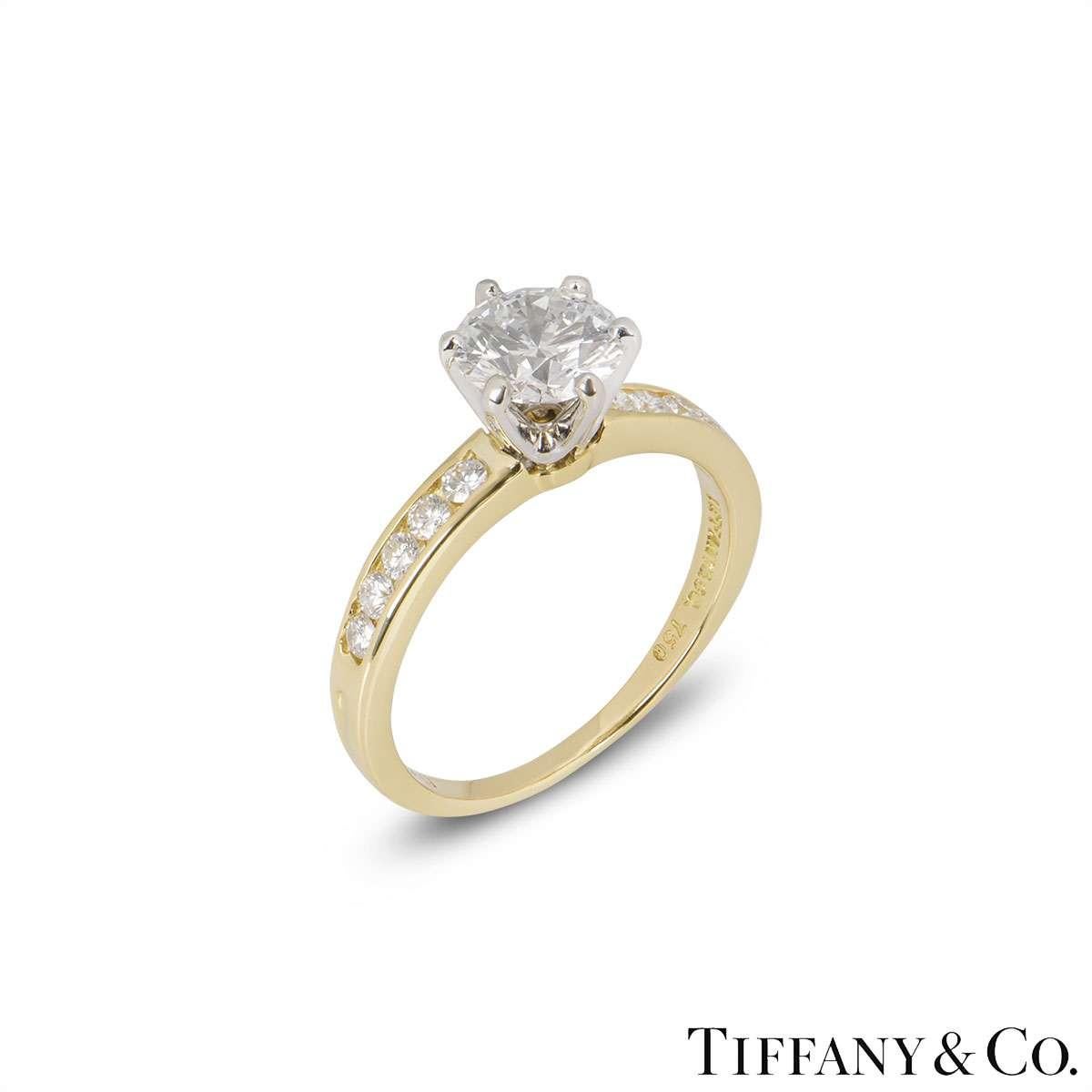 A stunning 18k yellow gold diamond ring by Tiffany & Co. The ring is set to the centre with a 1.08ct round brilliant cut diamond, H colour and VS1 clarity in a 6 claw setting. The shoulders are set with 10 round brilliant cut diamonds totalling