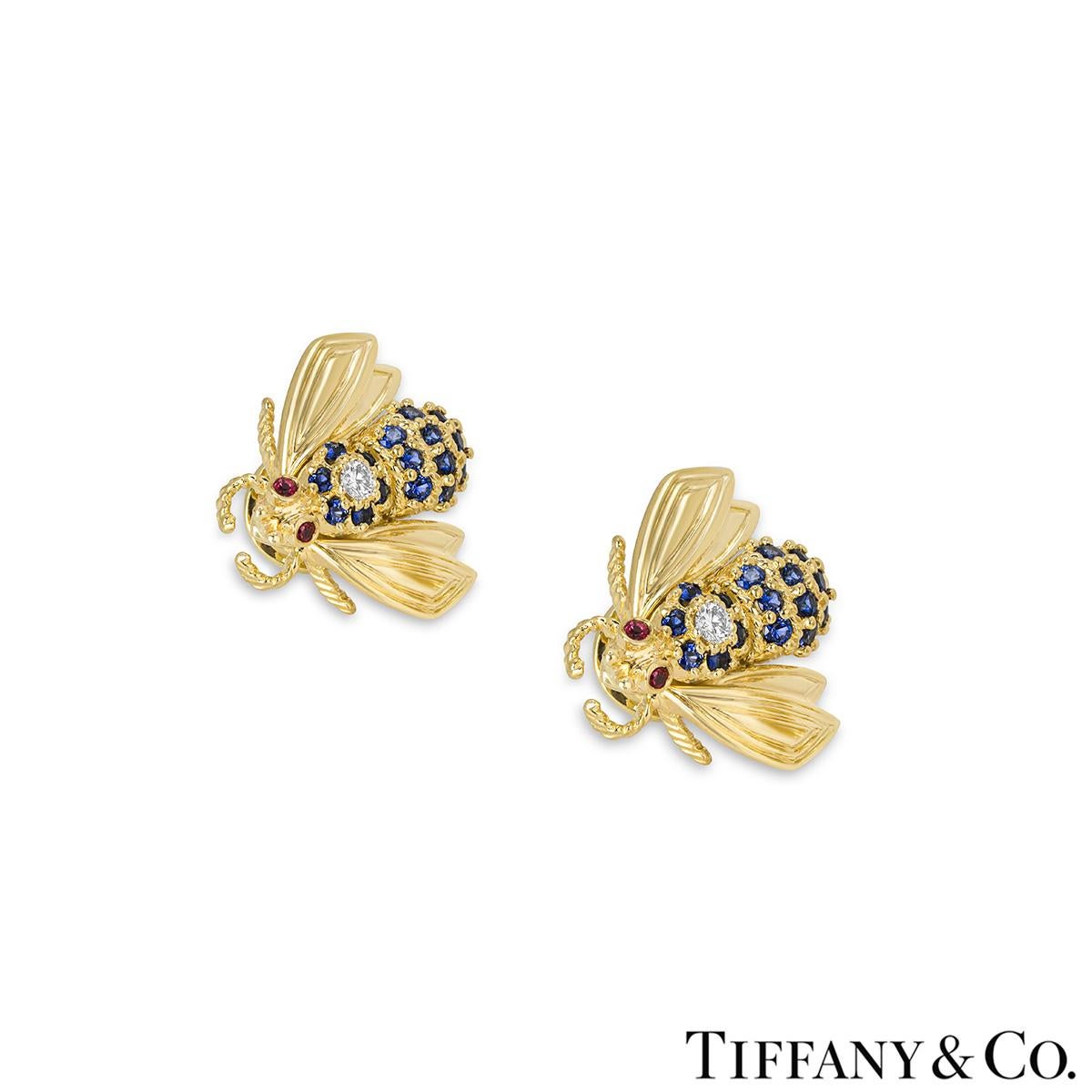 A charming pair of 18k yellow gold diamond, sapphire and ruby bee earrings by Tiffany & Co. The earrings each feature a bee motif set to the top of the body with a single round brilliant cut diamond, 16 round cut sapphires set throughout the body