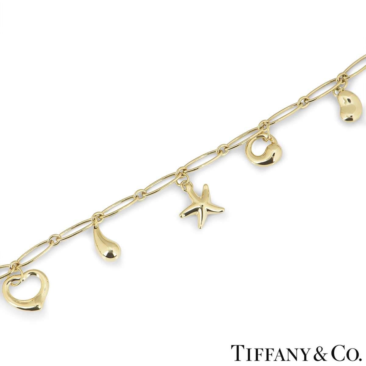 An 18k yellow gold charm bracelet from the Elsa Peretti collection by Tiffany & Co. The 5 charms include a bean motif, eternal circle, starfish, teardrop and open heart. The bracelet measures 7 inches in length, features a figure of eight clasp and