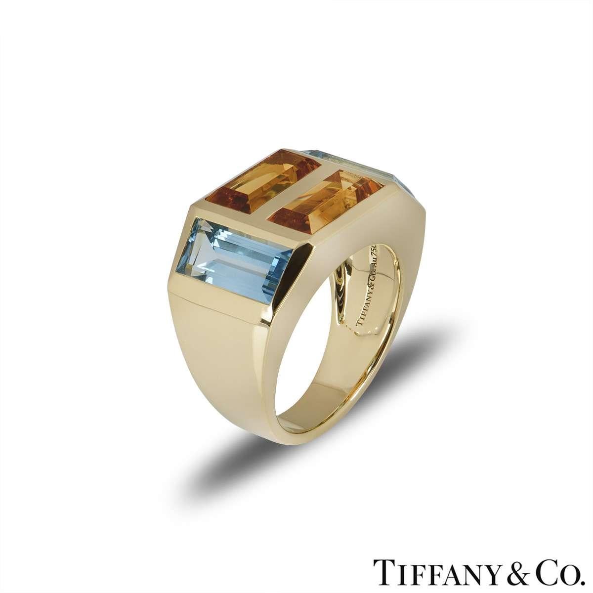 A beautiful 18k yellow gold dress ring from the Paloma Picasso collection by Tiffany & Co. The ring is set with two emerald cut citrine's set horizontally and two emerald cut blue topaz stones set vertically on either side. The citrine's have a