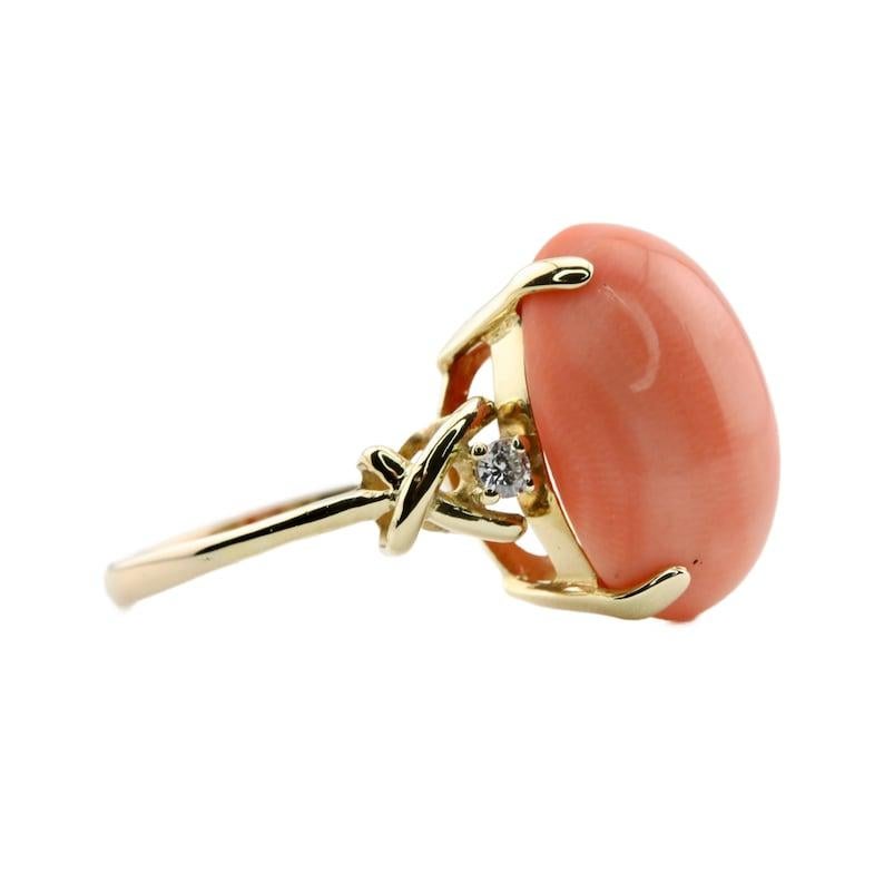 Aston Estate Jewelry Presents:

A vintage Tiffany & Company coral, and diamond three stone ring in 18 karat yellow gold. Centered by an Angel Skin coral cabochon measuring 17mm by 13mm and of beautiful peach color. Accenting the center coral are two
