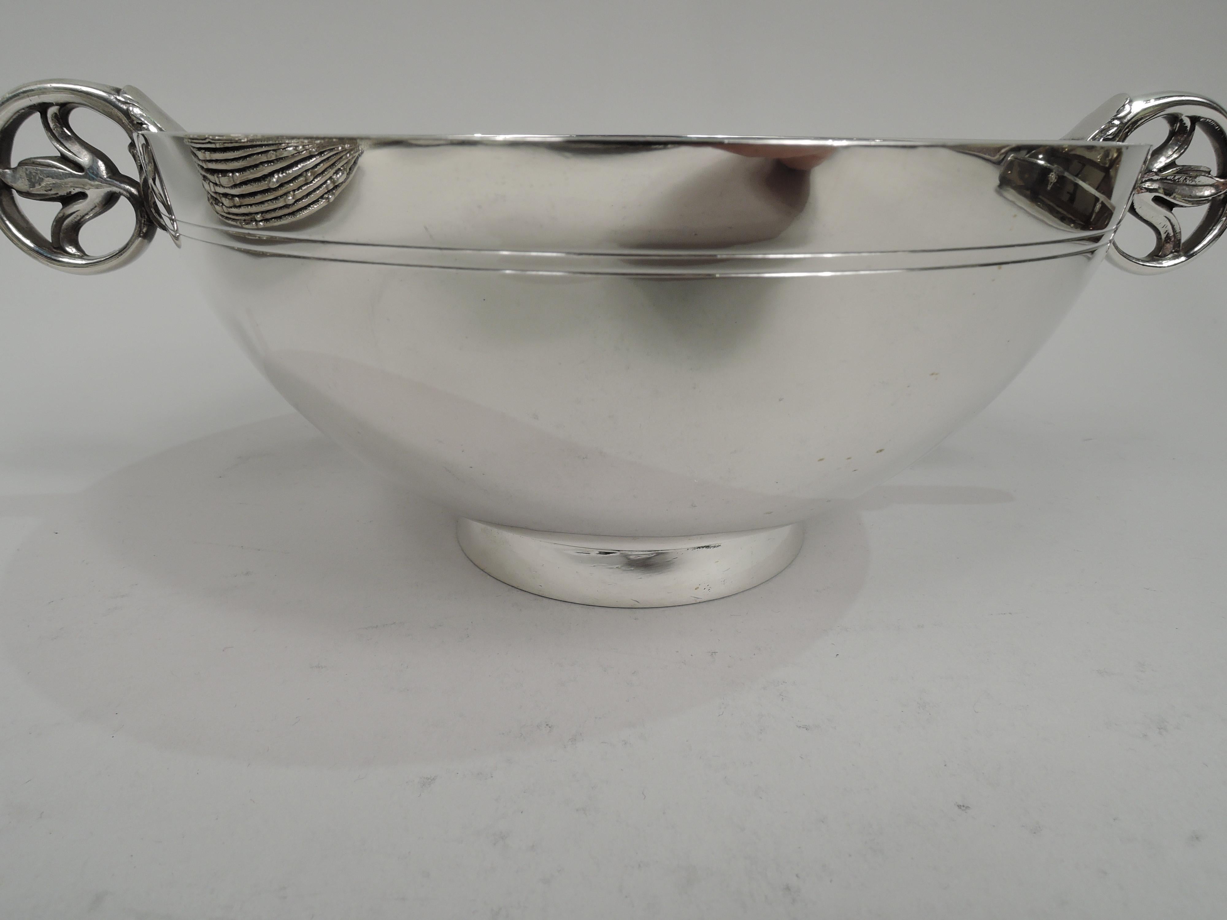 Modern sterling silver bowl. Made by Tiffany & Co. in New York, ca 1939. Round with curved and tapering sides with double tooled lines, and short and splayed foot. Leaf-capped volute-scroll side handles with interior trefoil terminal.