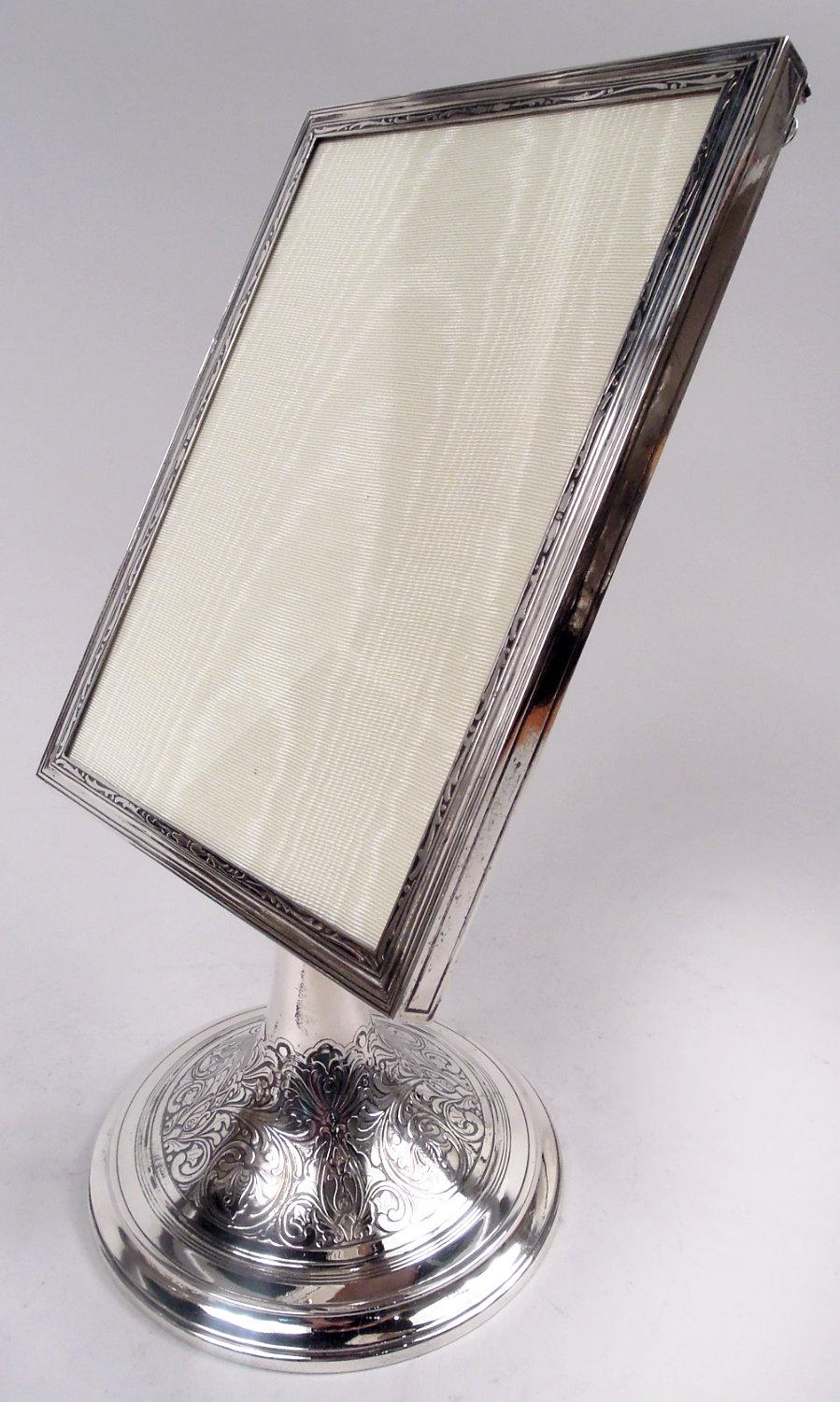 Edwardian Classical sterling silver picture frame. Made by Tiffany & co. in New York, ca 1915. Rectangular window in surround with incised borders on front and sides as well as acid-etched leafing scrolls on front. With glass, silk lining and
