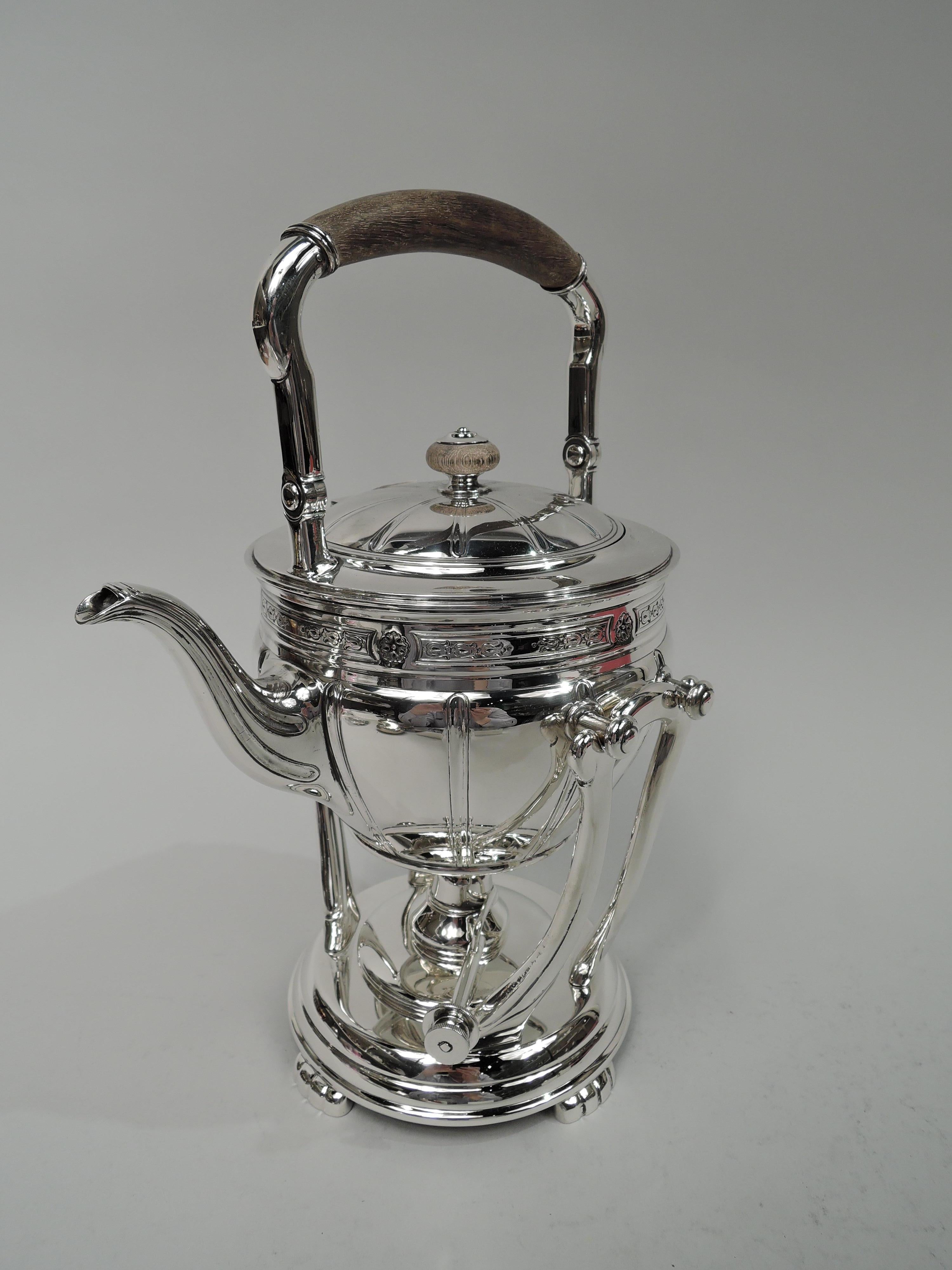 Edwardian Classical sterling silver hot water kettle on stand. Made by Tiffany & Co. in New York, ca 1908. Ovoid with flutes and ornamental border at rim comprising stylized flowers in tubular frames alternating with flower heads. Tapering s-scroll