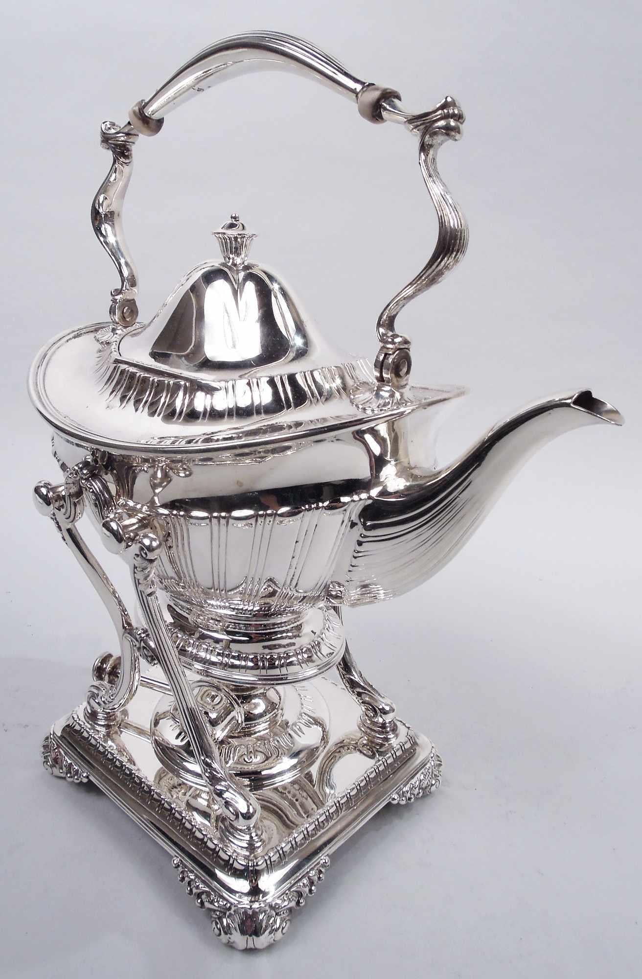 Edwardian Classical sterling silver tea kettle on stand. Made by Tiffany & Co. in New York, ca 1910. Kettle: Ovoid body on raised oval foot; lobed and domed side-hinged cover with vasiform finial. Swing-mounted scroll handle. Tapering and scrolled