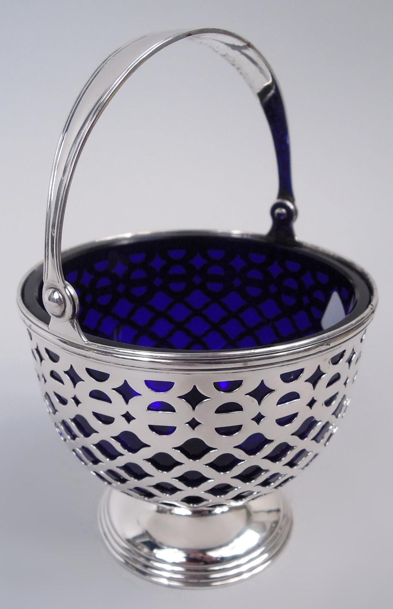 Edwardian Georgian sterling silver sugar basket. Made by Tiffany & Co. in New York, ca 1910. Bowl round and pierced; c-scroll swing handle and raised and stepped foot. Detachable cobalt blue glass liner. Fully marked including maker’s stamp, pattern
